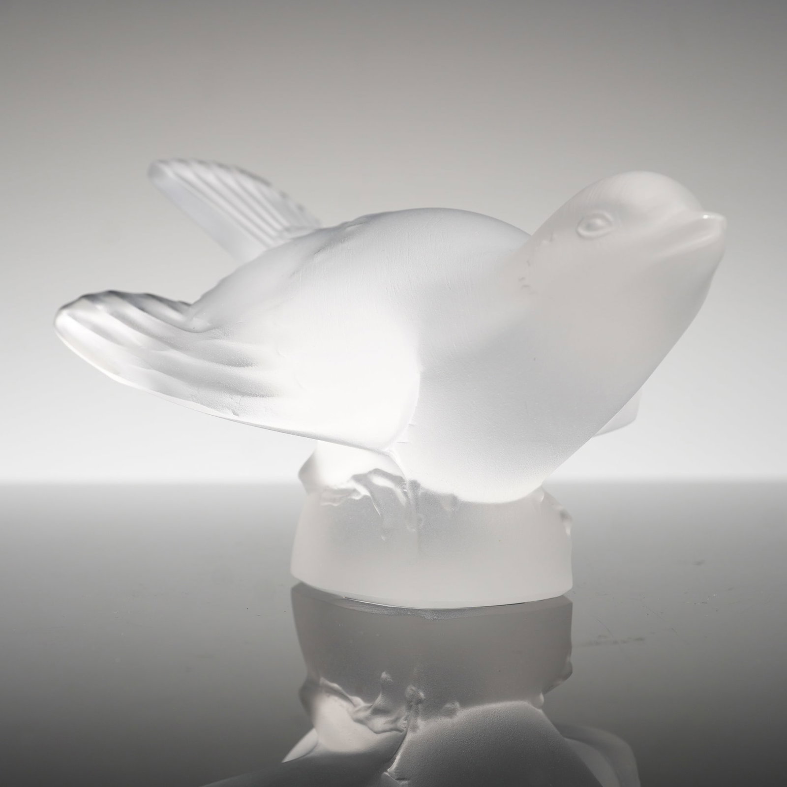 Lalique France Frosted Crystal Figurine, Sparrow: The bird is depicted with outstretched wings and its head turned upward. The piece is executed in a satin-finished crystal with an integral polished clear glass base. An etched signature reading Laliq