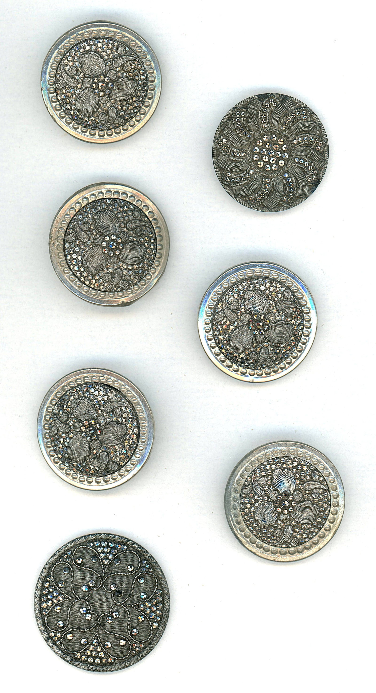 A SMALL CARD OF DIVISION ONE BLACK GLASS BUTTONS: 7 Medium/Large 19th century silver lustered examples. This lot includes 5 silver lustered black glass in metal and 2 non set in metal examples. All are in the lacy pattern style of glass and are stunn