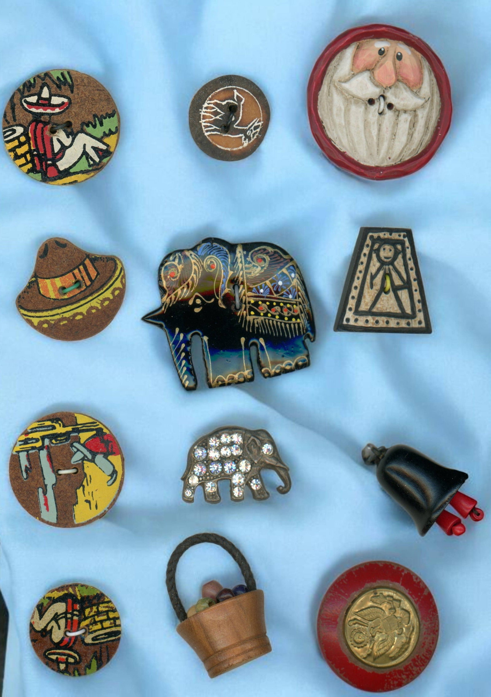 A SMALL CARD OF DIVISION 3 ASSORTED MATERIAL BUTTONS: 12 Medium 20th century examples including wood & linoleum. This lot includes several hand painted examples along with a nice realistic jeweled elephant, a colorful Bakelite elephant, a carved and pain