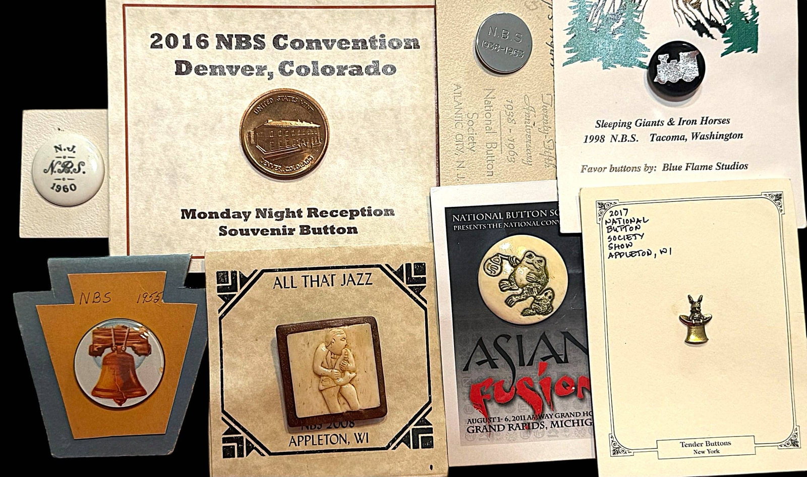 A SELECTION OF DIVISION THREE NBS FAVOR BUTTONS: 8 Medium/Large 20th/21st century assorted examples. This nice selection includes A Will Stokes foil train paperweight from the 1998 Tacoma Washington Convention, a large square wood and =bone Musician