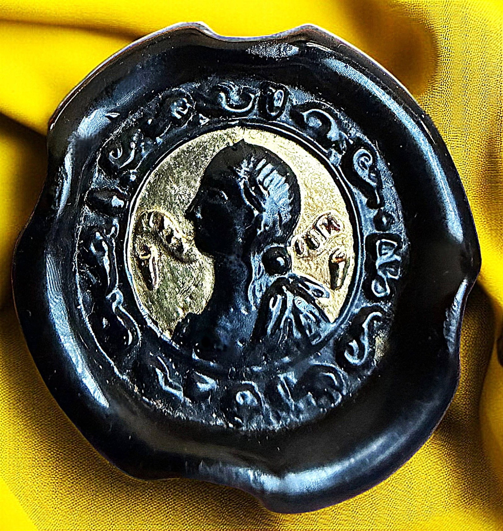 A DIVISION THREE BLACK GLASS PICTORIAL BUTTON: 1 Large 1940's black and gold lustered English Bimini glass. Here we have a Bimini glass in black glass with a gold lustered profile head in a coin like style. The typical Bimini back and shank is unm