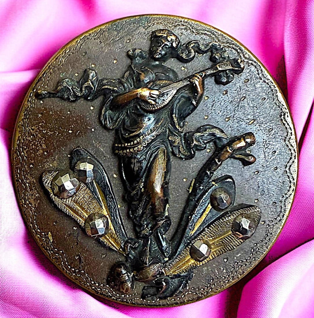 A DIVISION ONE BRASS PICTORIAL FIGURAL BUTTON: 1 Large 19th C. lady playing a mandolin and riding a dragonfly. This detailed and fine quality brass pictorial shows the women and dragonfly in high relief. Set with cut steels accenting the design. T