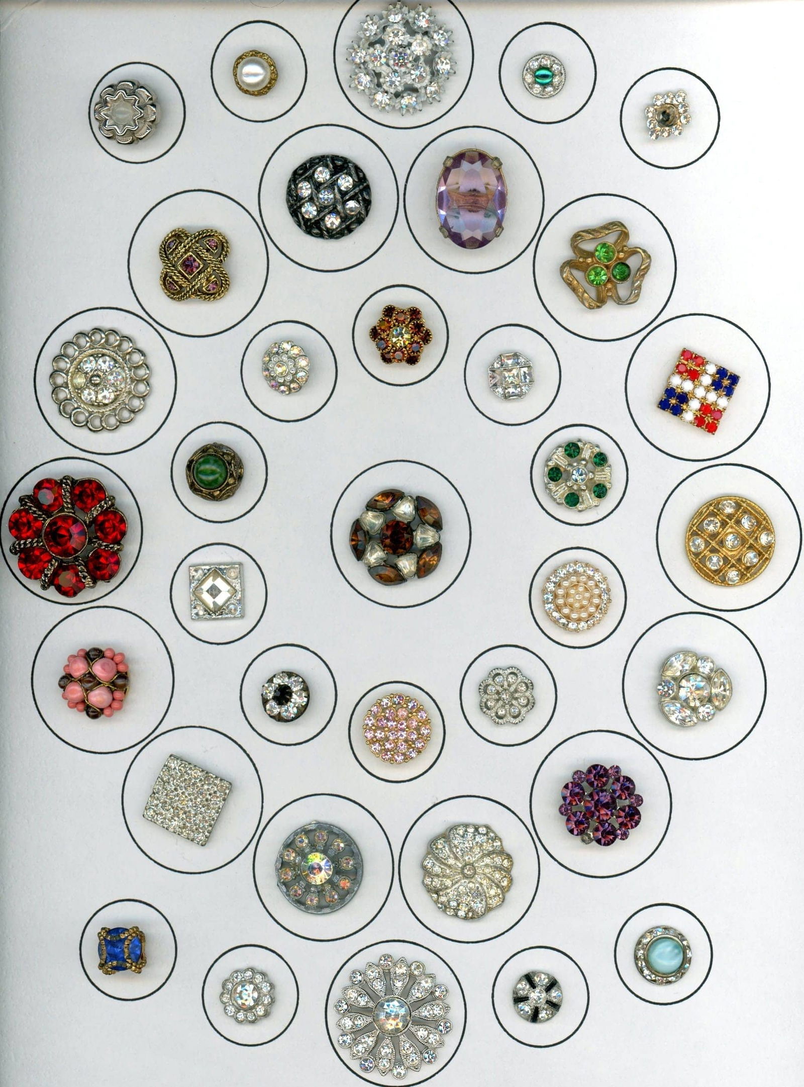 A CARD OF DIVISION THREE "GLITZ" BUTTONS: 35 S/M/L Mid 20th century colorful paste jewel examples. Here is a card of a variety of shapes and clear and or colored glass stones in metal that imitate gemstones. A sparkling array of buttons. Dime