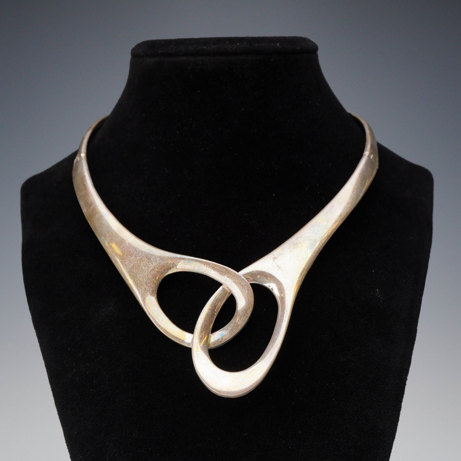 Sterling Silver Modernist Hinged Collar Necklace with Interlocking Loop Centerpiece: This sterling silver collar necklace exemplifies the mid-century modernist aesthetic through its fluid, biomorphic lines and asymmetrical design. Crafted in Taxco, Mexico, the piece features a bold ce