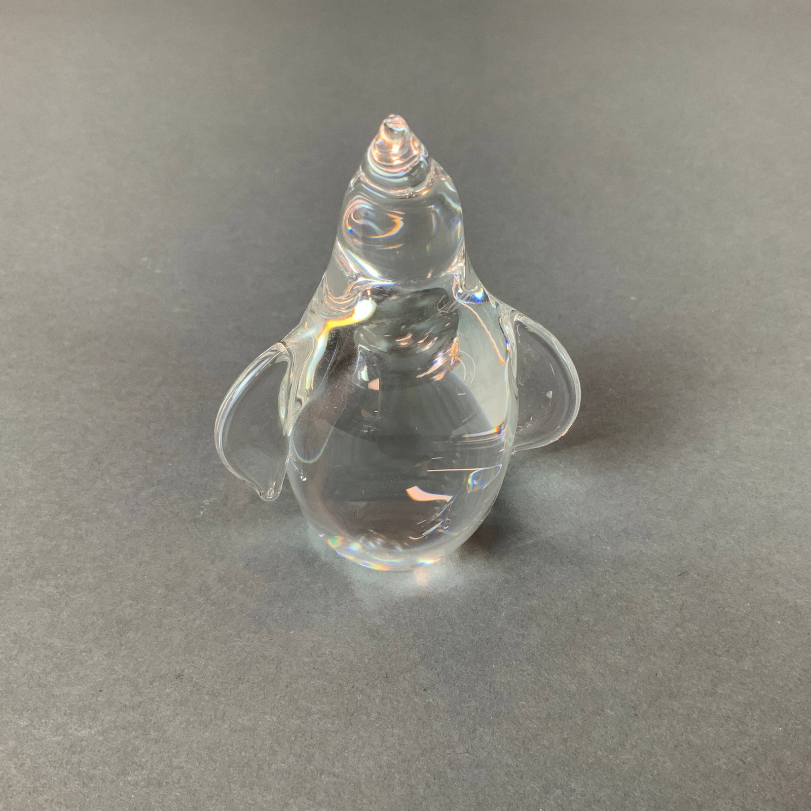 Steuben Crystal Penguin Figurine: A Steuben crystal penguin figurine. This stylized animal figure is crafted from clear, solid lead glass. The minimalist design features a rounded body with two small pulled-out wings and a tapering he