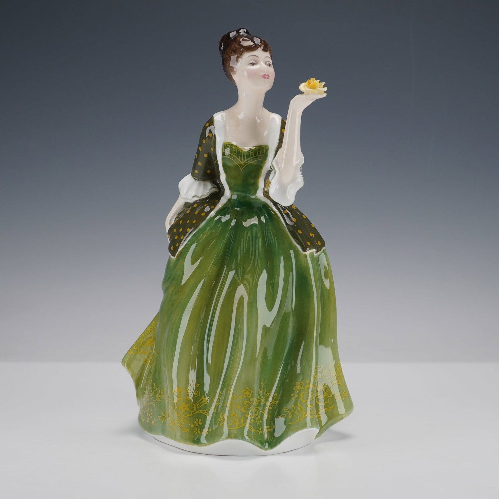 Royal Doulton Figurine, Fleur HN2368: Bone china figure depicted standing with one arm gracefully extended while holding a yellow blossom, wearing a layered gown in graduated tones of olive and chartreuse with yellow floral embellishments