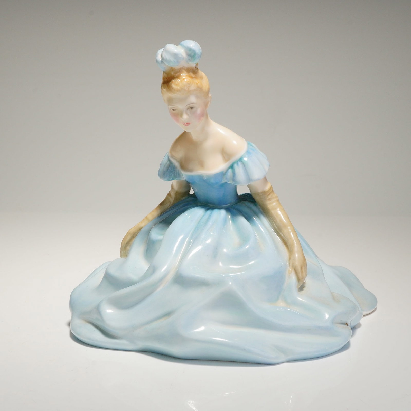 Royal Doulton Figurine Debutante HN4434: A glazed porcelain figurine titled "Debutante," model number HN 4434, produced by Royal Doulton. The figure depicts a young woman kneeling, dressed in a voluminous, ruffled, off-the-shoulder ballgown