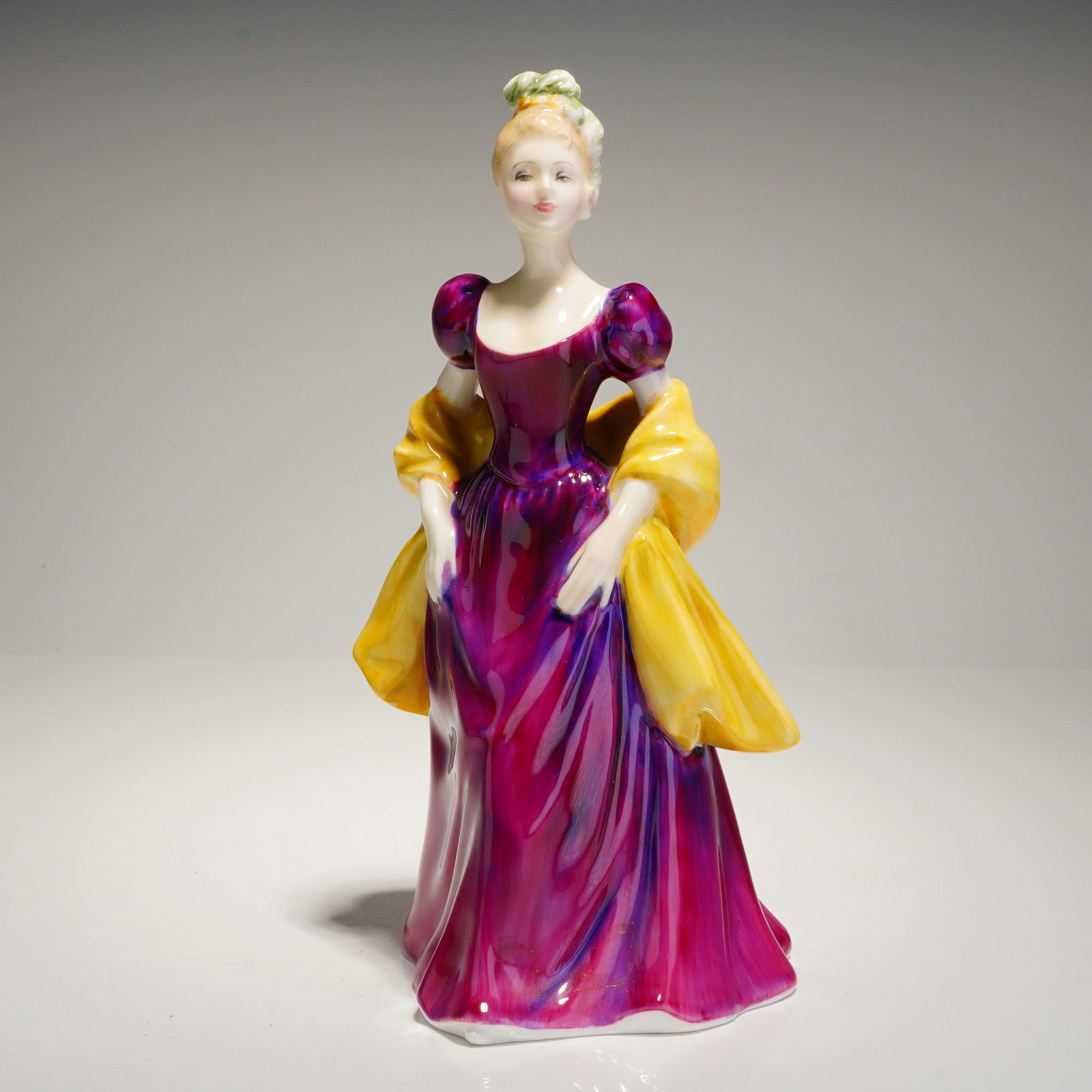 Royal Doulton Figurine Loretta HN2337: A glazed bone china figurine manufactured by Royal Doulton, titled Loretta, model number HN 2337. The figure depicts a standing woman dressed in a full-length gown rendered in vibrant magenta and purp