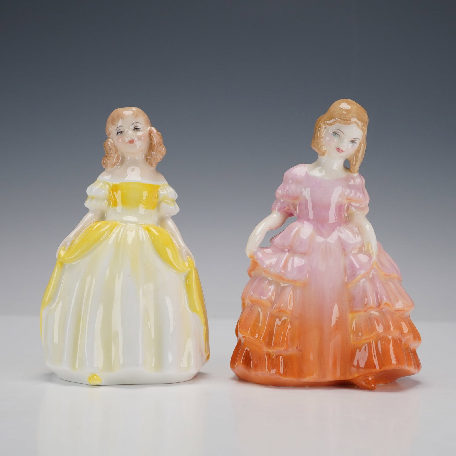 2pc Royal Doulton Figurines, Penny and Rose: Two hand-painted porcelain figures comprising Penny HN2424 and Rose HN1368. Penny is modeled wearing a yellow gown while Rose is depicted in graduated pink and orange ruffled dress; each modeled as a