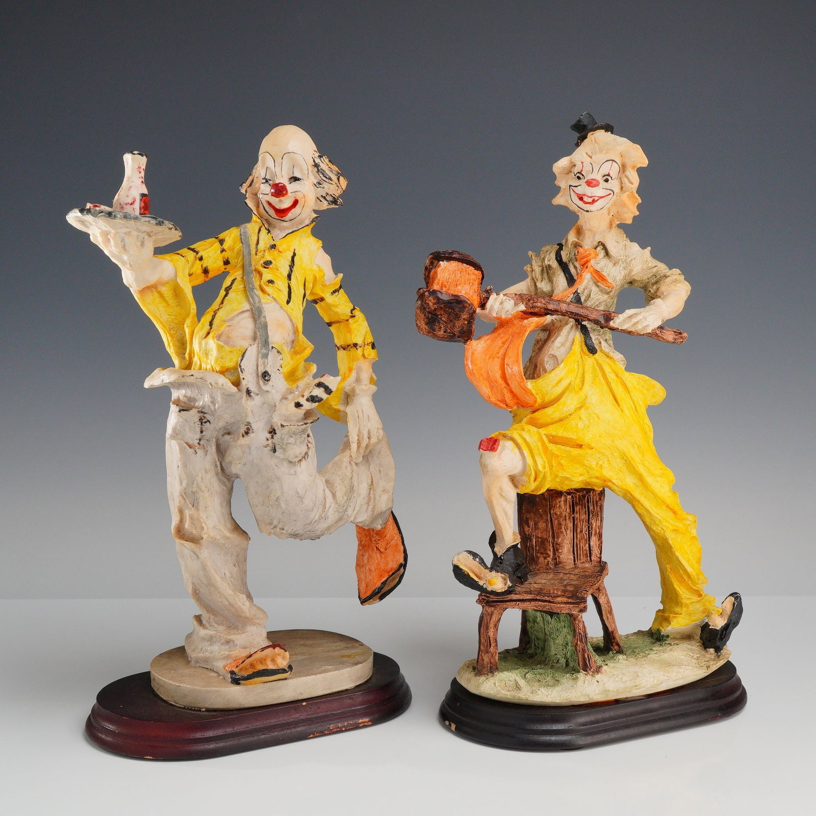 Dante by Ado for Creative World, A Pair of Clown Figurines: A pair of Dante by Ado clown figurines produced for Creative World, featuring two expressive and whimsical characters. The first figure depicts a waiter in a dynamic balancing pose, holding a circular