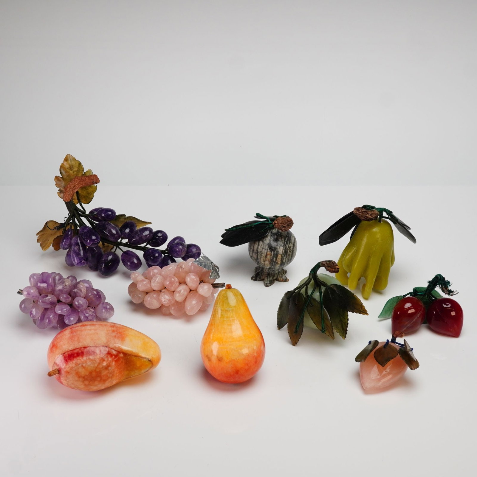 Collection of Ten Chinese Carved Hardstone Fruit Specimens: A collection of ten hand-carved semi-precious hardstone fruit specimens, likely of Chinese origin, Mid-Century Modern period (c. 1950s-1970s). The assembly includes three clusters of grapes in amethys