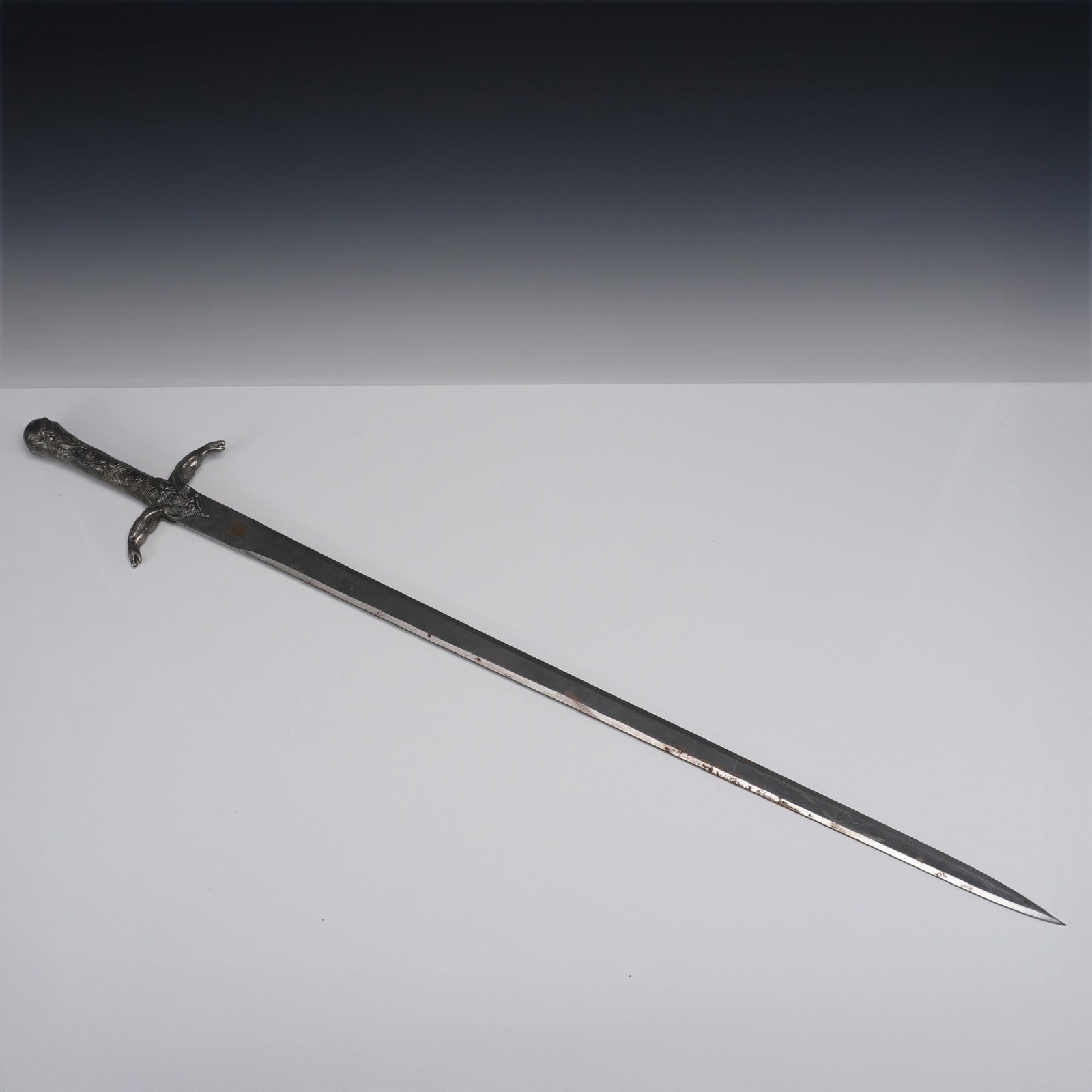 Coyote Cutlery Fantasy Sword With Sculpted Handle: Fantasy sword marked Coyote Cutlery, featuring a long stainless blade with squared tip and visible wear along the edge. The cast metal grip is decorated with detailed raised figures, including a centr