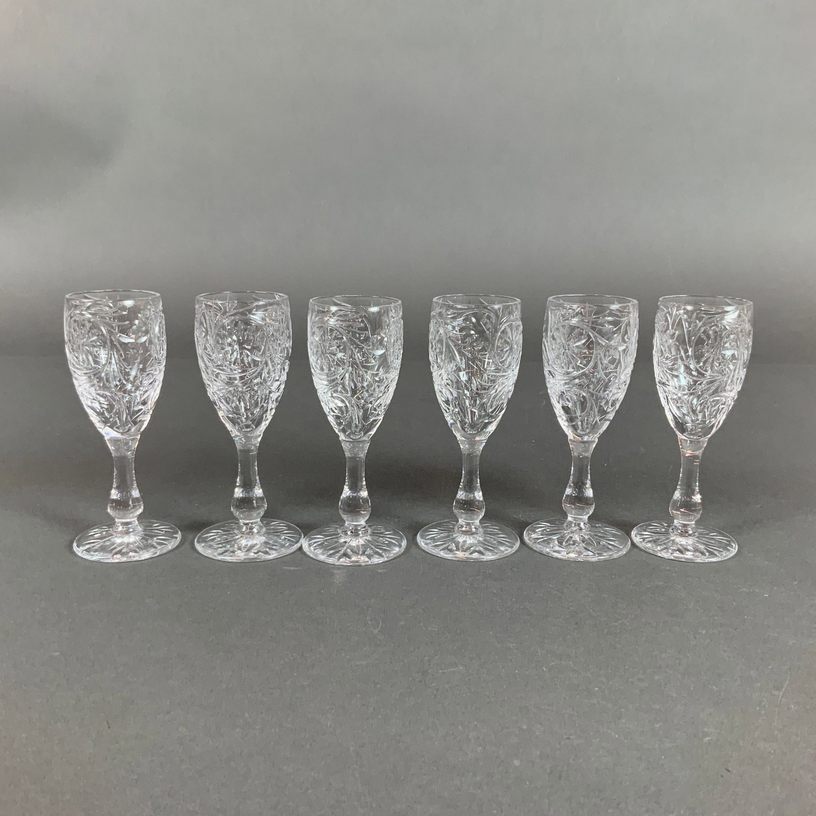A Set of Six Tudor England Cut Crystal Liqueur Glasses: This set of six liqueur glasses is attributed to Tudor Crystal, England. Each glass is crafted from hand-cut lead crystal and features a tulip-shaped bowl supported by a baluster stem with a central k