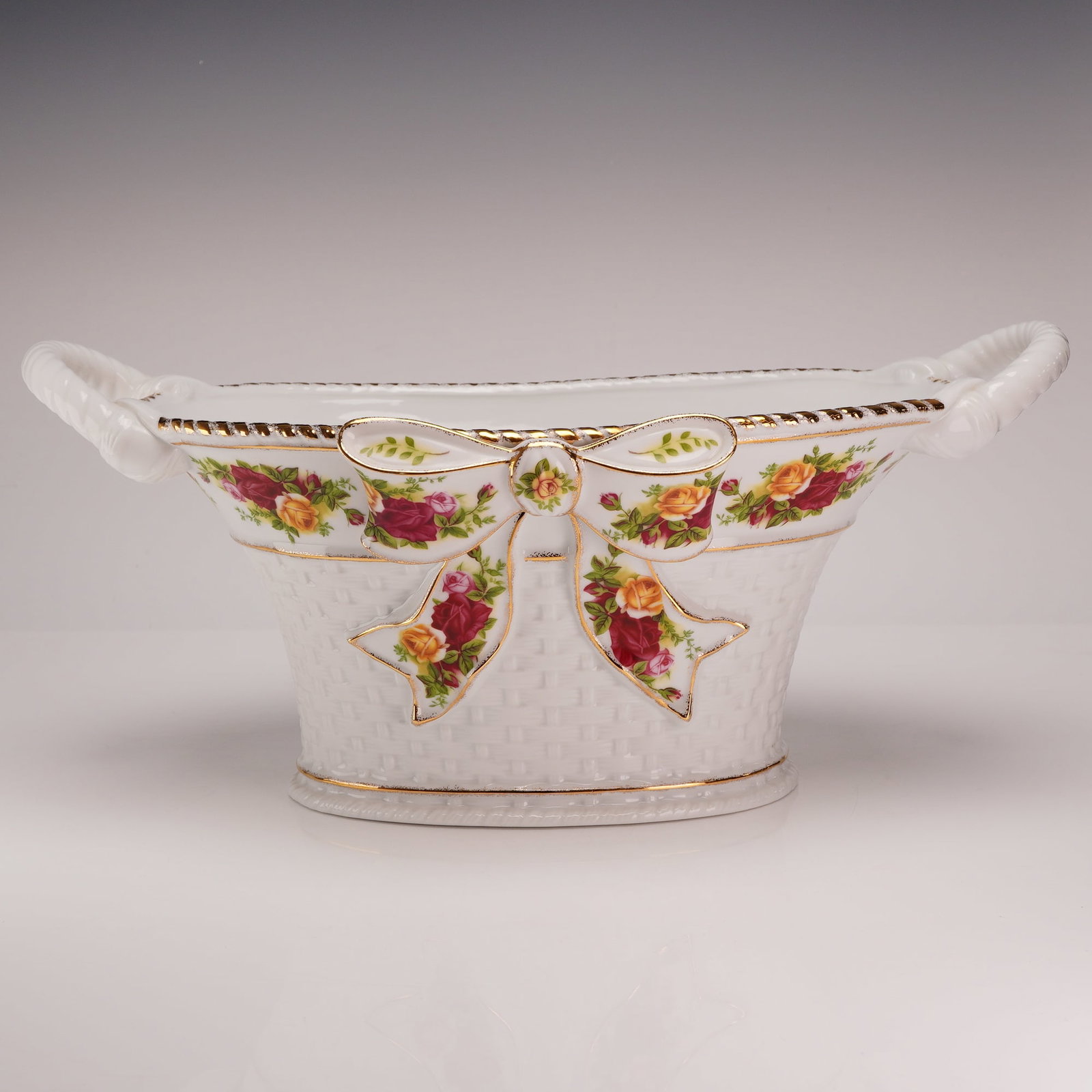 Royal Albert Old Country Roses Bone China Centerpiece Basket: A Royal Albert fine bone china centerpiece basket in the Old Country Roses pattern. The vessel is oval in form with a flared rim featuring a gadrooned edge. It is constructed with two twisted rope-sty