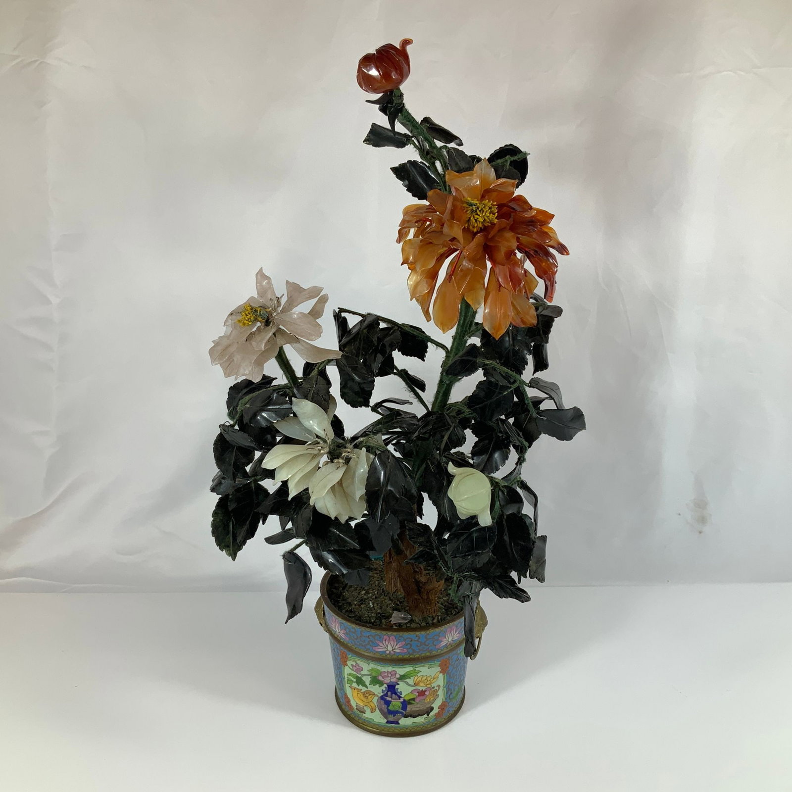 Chinese Carved Gemstone Tree in Cloisonne Enamel Pot: This decorative gemstone tree features hand-carved semi-precious stone blossoms and foliage. The flowers include an amber-toned blossom, a translucent pale pink flower, and white buds. The leaves are