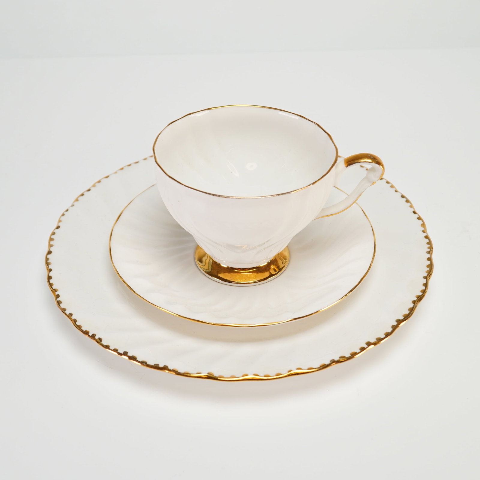 Vintage Queen Anne and Gladstone Bone China Tea Trio Set of 3 with Gold Accents: This three-piece set consists of a teacup, saucer, and side plate manufactured in England from fine bone china. The pieces feature a matching design characterized by a white ground with molded swirl f