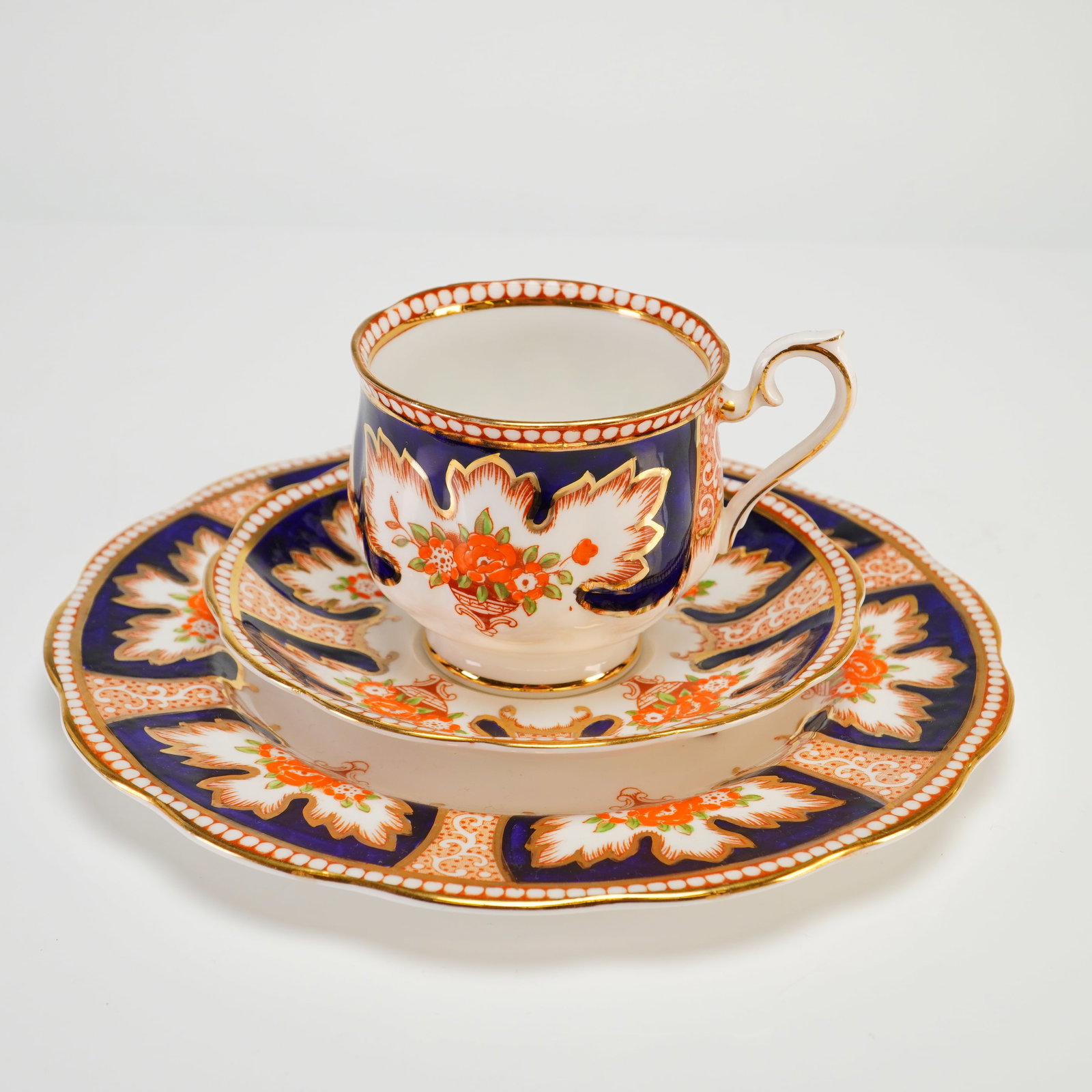 Vintage Royal Albert Royalty Series Bone China Tea Trio Set of Three: This vintage Royal Albert bone china tea trio from the Royalty series includes a footed teacup, a saucer, and a side plate. The set features an Imari-inspired design with alternating panels of deep co
