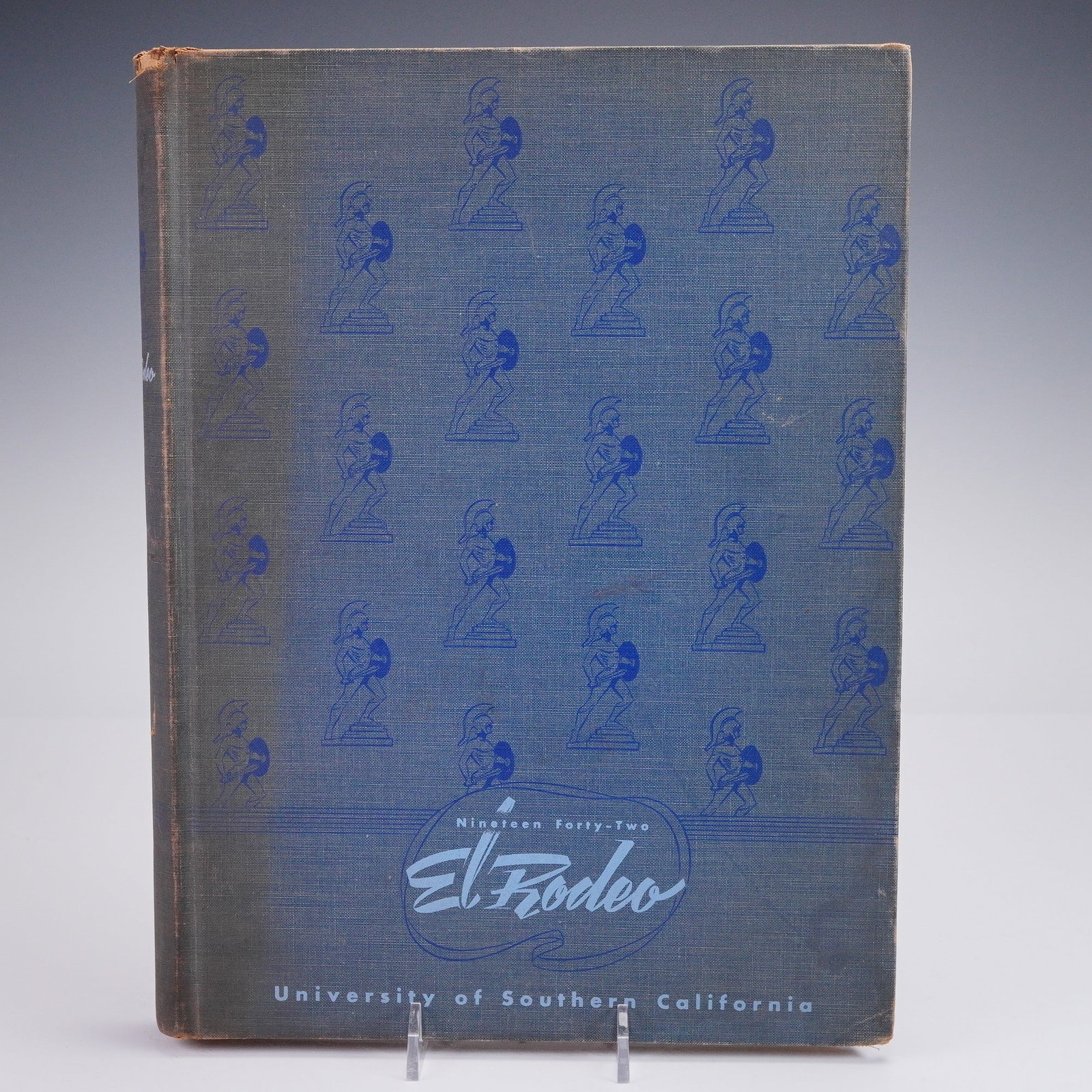 1942 University of Southern California El Rodeo Yearbook: 1942 edition of El Rodeo, the official yearbook of the University of Southern California. Hardcover with embossed Trojan warrior motif across the cloth boards. Includes photographs and writeups docume