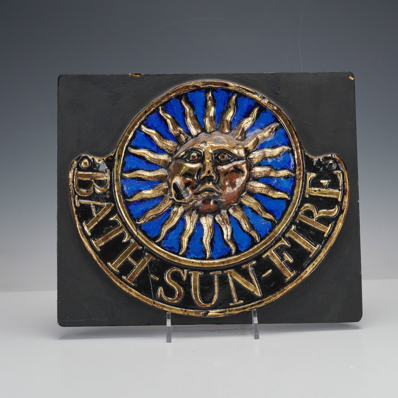 Reproduction Fire Mark Plaque for the Bath Sun Fire Office: A rectangular reproduction plaque depicting the fire mark of the Bath Sun Fire Office. The piece features a central raised sun motif with a human face, rendered in gilded gold and oxidized colors agai