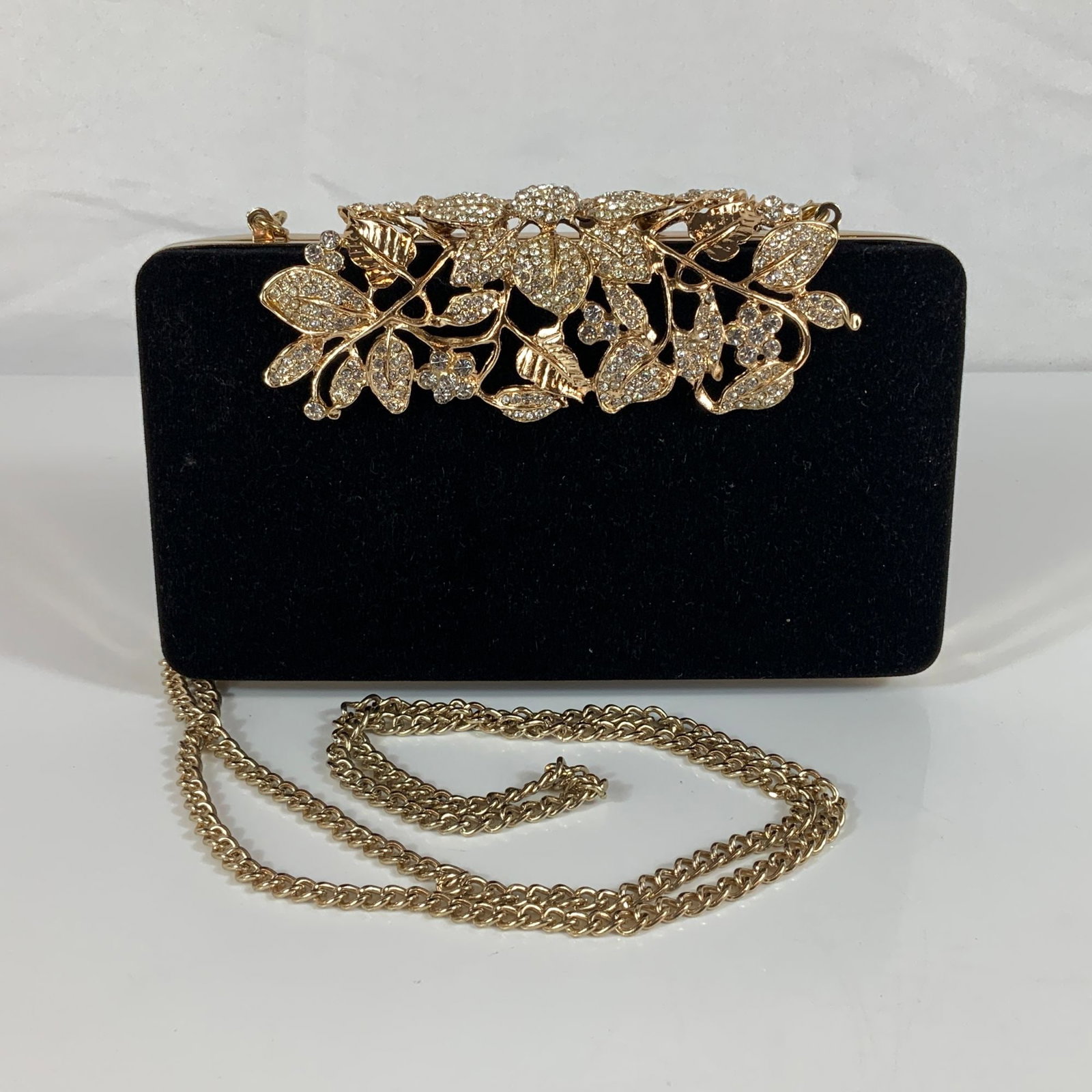 Dexmay Rhinestone Encrusted Floral Velvet Evening Clutch Bag: This rectangular box-style evening clutch is produced by Dexmay. The exterior is constructed from a black velvet-textured fabric. The front of the bag features a gold-tone metal filigree overlay desig