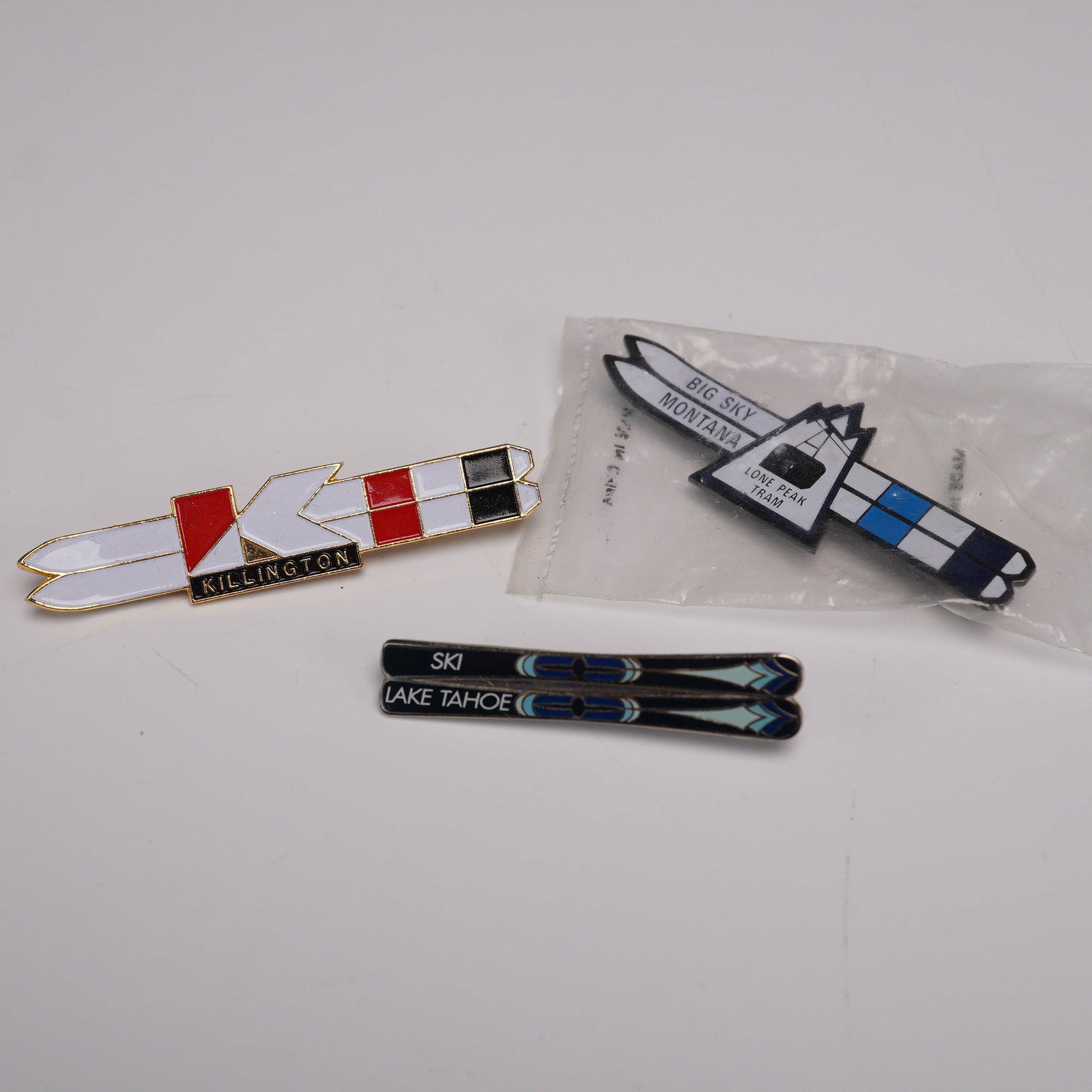 3pc Ski Resort Enamel Pins, Killington, Big Sky, Lake Tahoe: Group of three enamel ski pins featuring various North American ski resorts. Includes a Killington pin designed as crossed skis in red, white, and black; a Big Sky Montana "Lone Peak Tram" pin in orig
