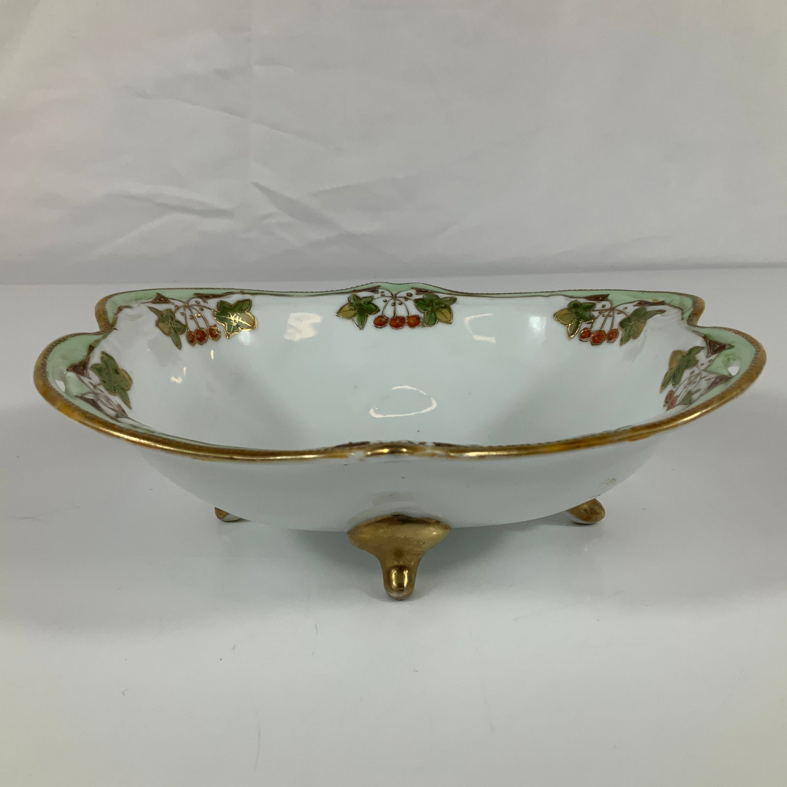 Vintage Noritake Hand Painted Footed Porcelain Nut Bowl with Floral Design and Gold Trim: This vintage footed porcelain bowl features a lobed form with a scalloped and pierced rim. The interior decoration consists of a light green border accented by hand-painted clusters of red berries and