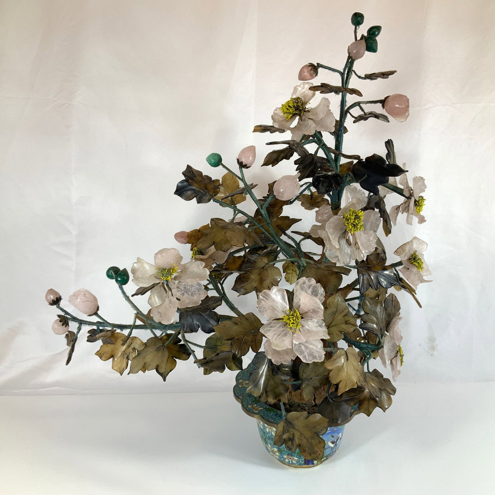 Chinese Hardstone and Rose Quartz Gemstone Tree in Cloisonne Enamel Planter: A Chinese gemstone tree, also known as a hardstone bonsai, featuring blossoms carved from translucent pale pink rose quartz with yellow-tipped stamens. The foliage is composed of multi-lobed leaves ca