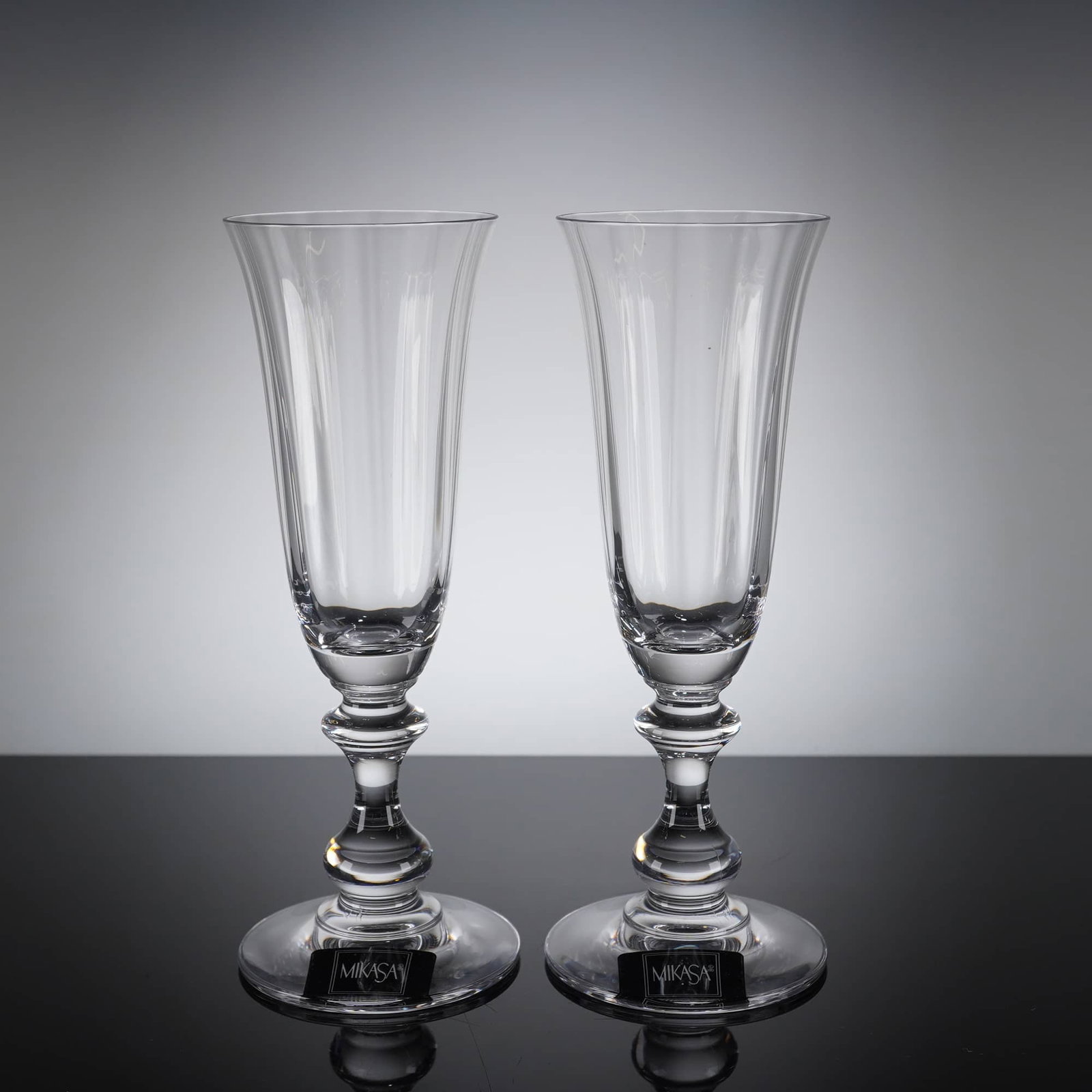 2pc Mikasa French Countryside Champagne Flutes: A pair of champagne flutes manufactured by Mikasa in the "French Countryside" pattern. The glasses are crafted from clear crystal and feature a tall, slender bowl with subtle vertical faceting around