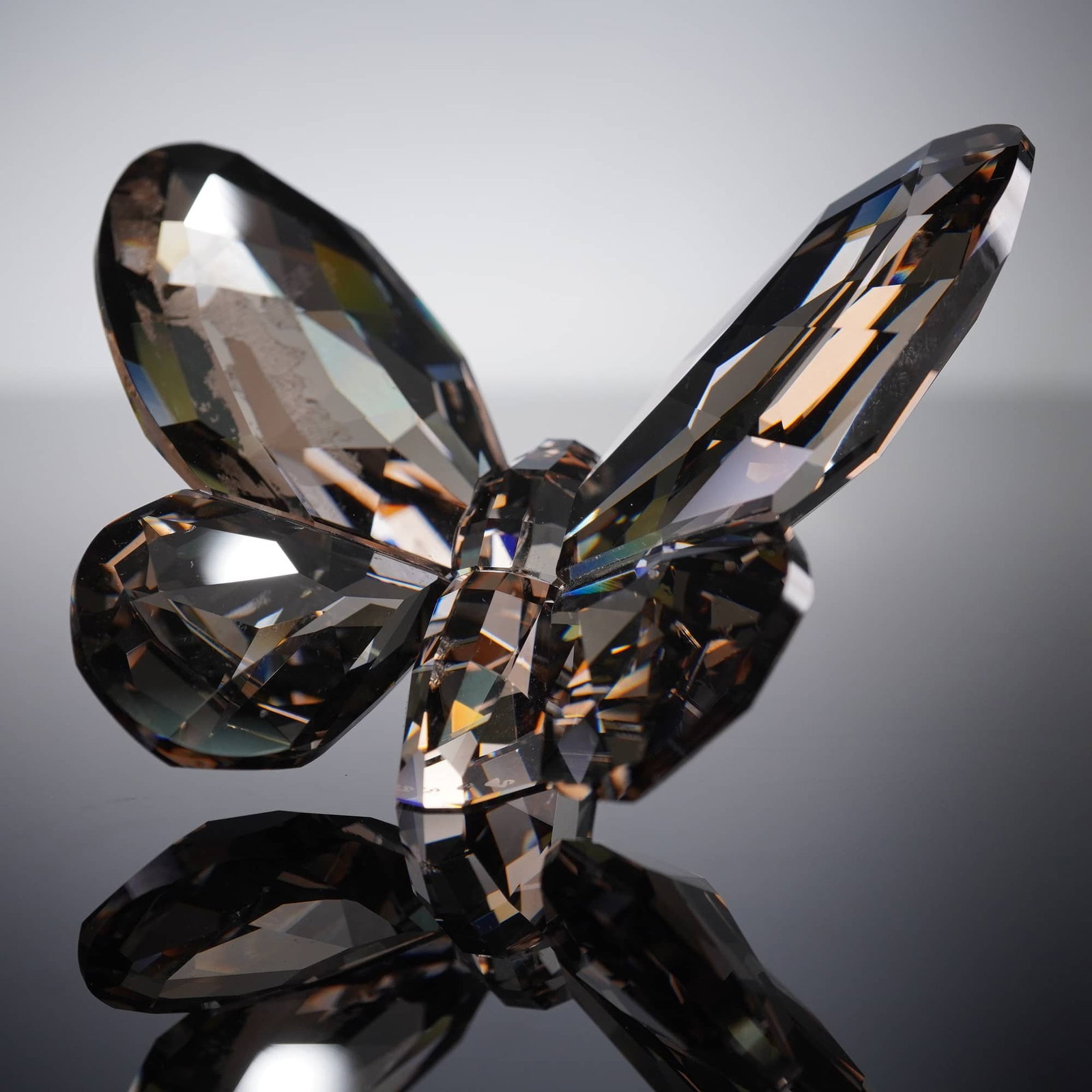 Swarovski Satin Butterfly Faceted Crystal Paperweight Figurine: A Swarovski 'Satin Butterfly' faceted crystal paperweight figurine. Crafted from faceted crystal, exhibiting a smoky or champagne hue that reflects light. The object comprises a central body and four