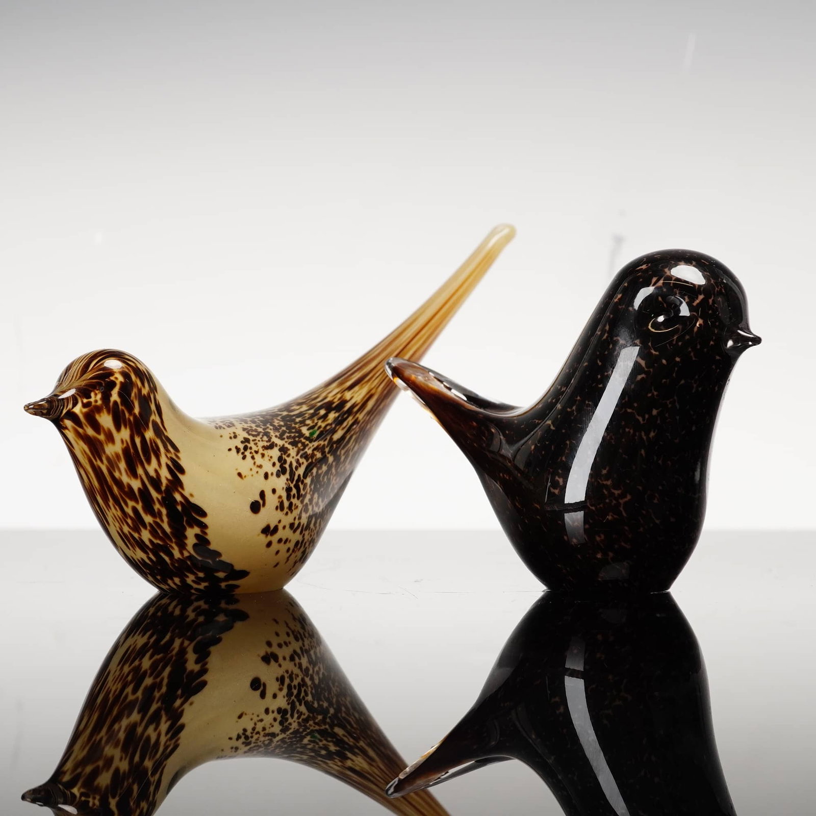 2pc Wedgwood Art Glass Bird Figurines: This pair of stylized Wedgwood glass bird figurines includes one slender upright form and one compact rounded songbird. Both pieces feature a mottled tortoiseshell or macchia pattern, with the taller 