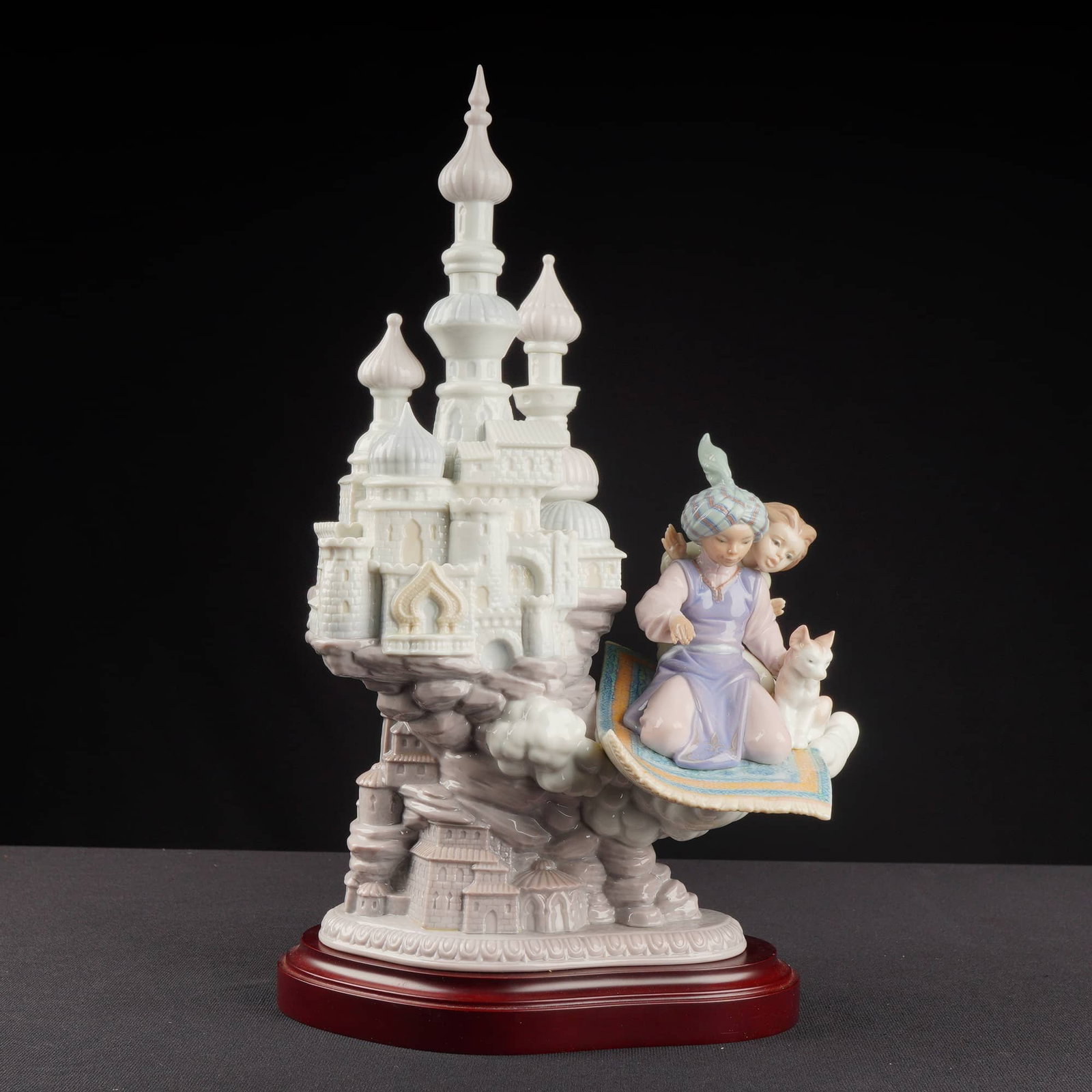 Lladro Porcelain Sculpture Dreams of Aladdin 01006285 with Base: The sculpture depicts a complex, fantastical scene featuring a tiered, multi-turreted castle structure rendered primarily in white and pale lavender glaze, rising above clouds. Resting upon the clouds