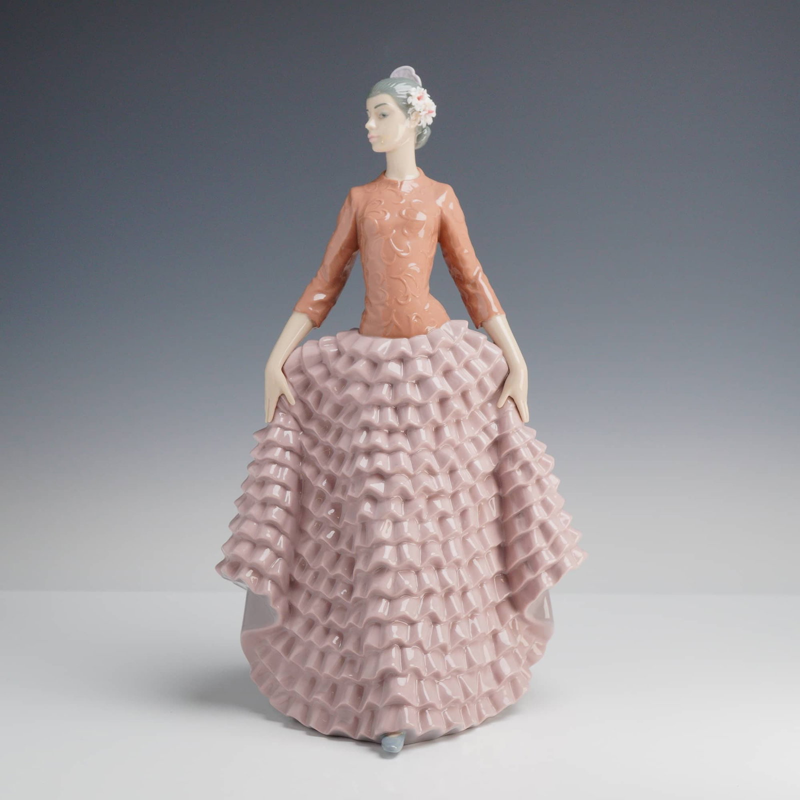 Lladró "Fiesta Dancer" Glazed Porcelain Figurine 6163: This Lladró glazed porcelain figurine is titled Fiesta Dancer, model number 6163. Designed by sculptor Juan Huerta, the piece features a sophisticated female figure in an elegant pose, holding the ed