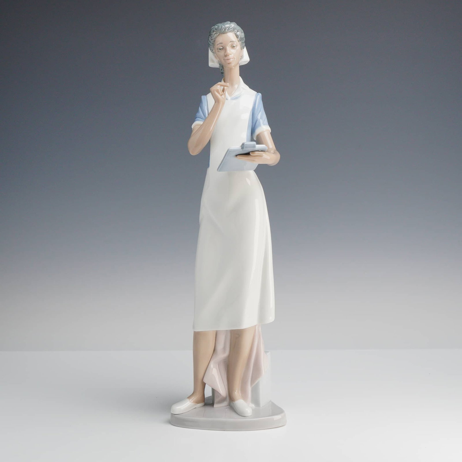 Lladró, Making Rounds Nurse Figurine: A fine glazed porcelain Lladró sculpture titled Making Rounds (model number 6256), also known as the African American Nurse. The figure depicts a woman in a traditional mid-century nursing uniform, i