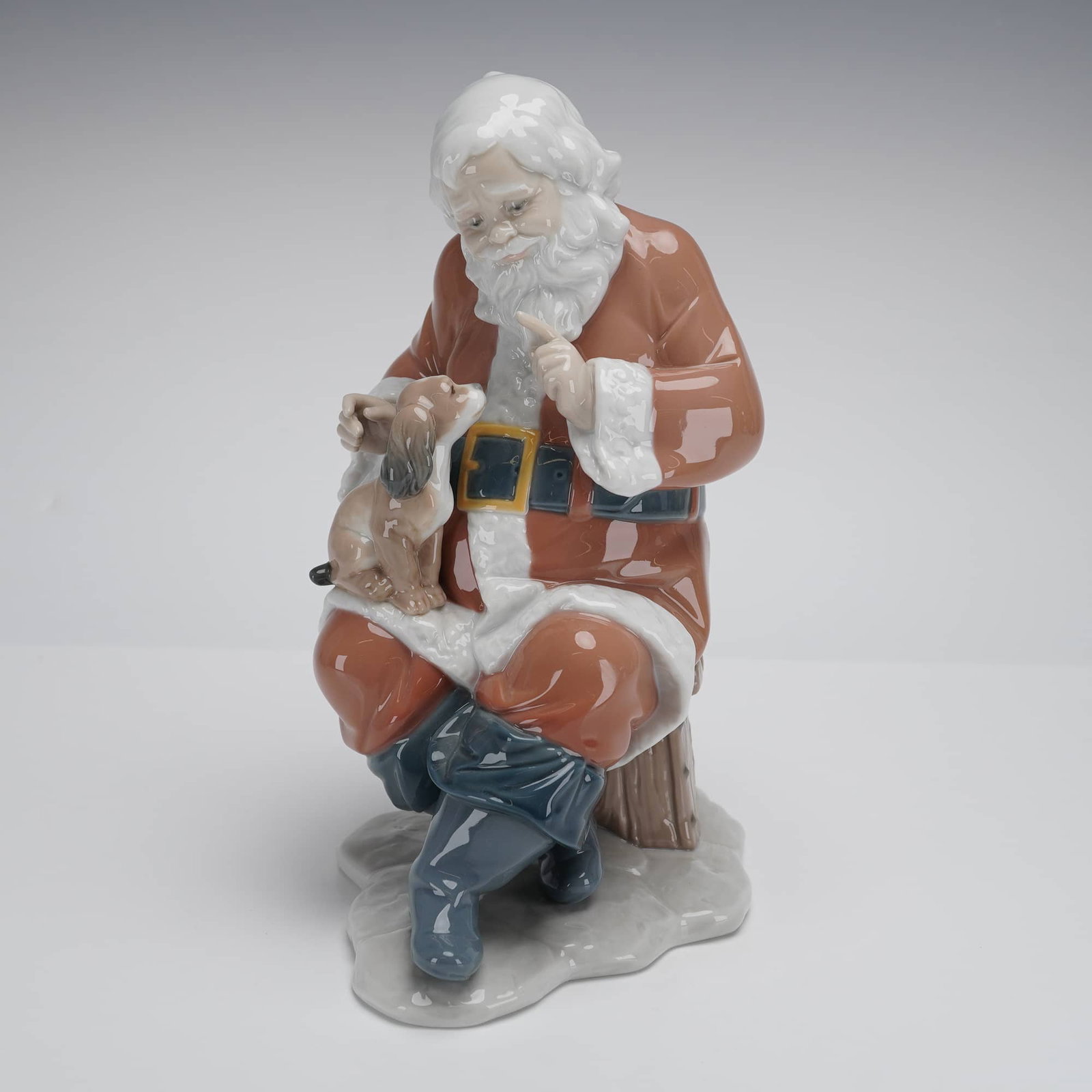 Lladro Porcelain Figurine, Santa's Little Secret 1006890: A Lladro Figurine Santa's Little Secret (model 6890) designed by Virginia Gonzalez. It depicts a glossy reddish-brown porcelain Santa Claus seated on a stool with a small dog, marked LLADRO and DAISA