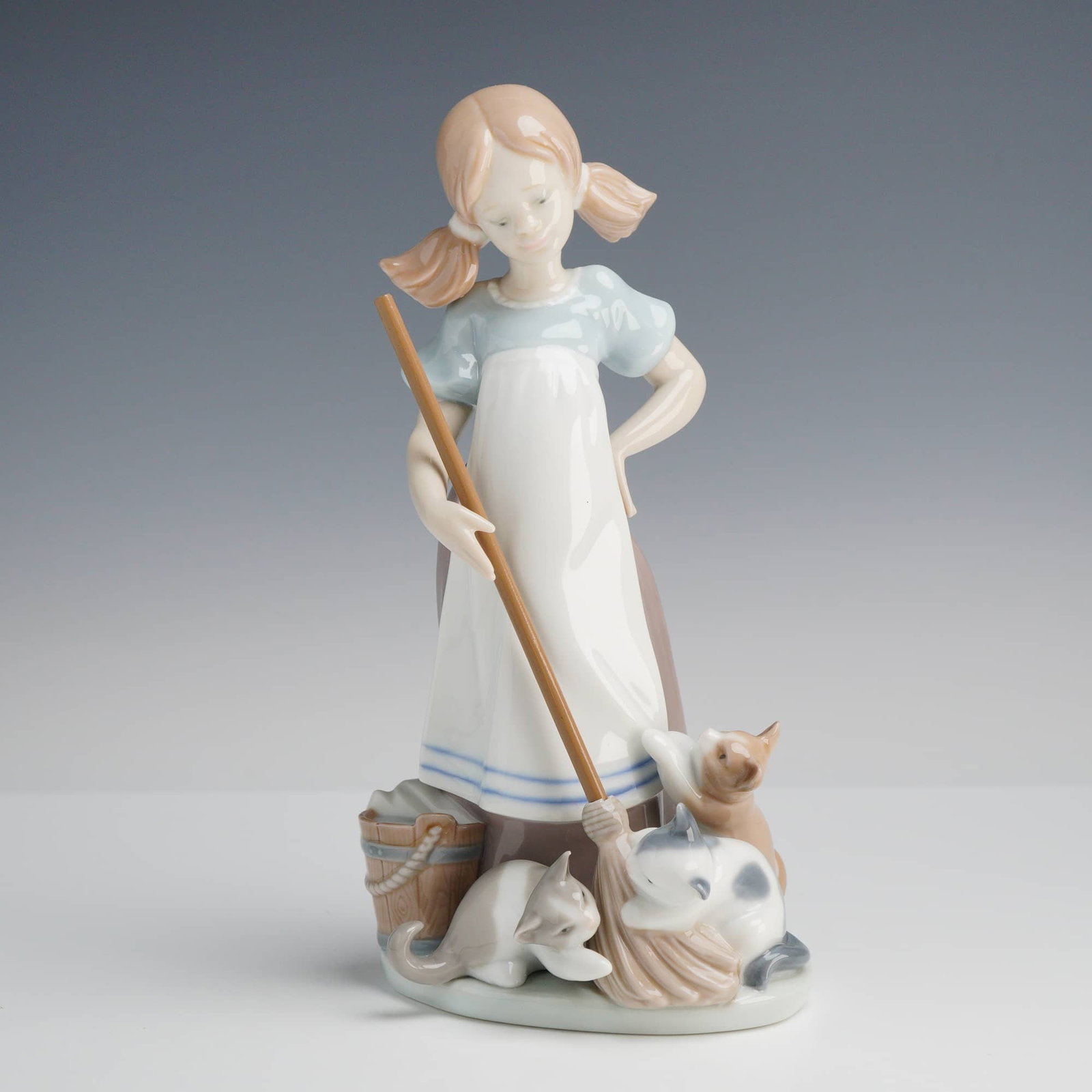 Lladro, Playful Kittens Figurine #5232: A glazed porcelain Playful Kittens Lladró figurine, model number 5232, designed by sculptor Juan Huerta. This charming piece depicts a young girl with blonde pigtails in a pensive pose, holding a bro