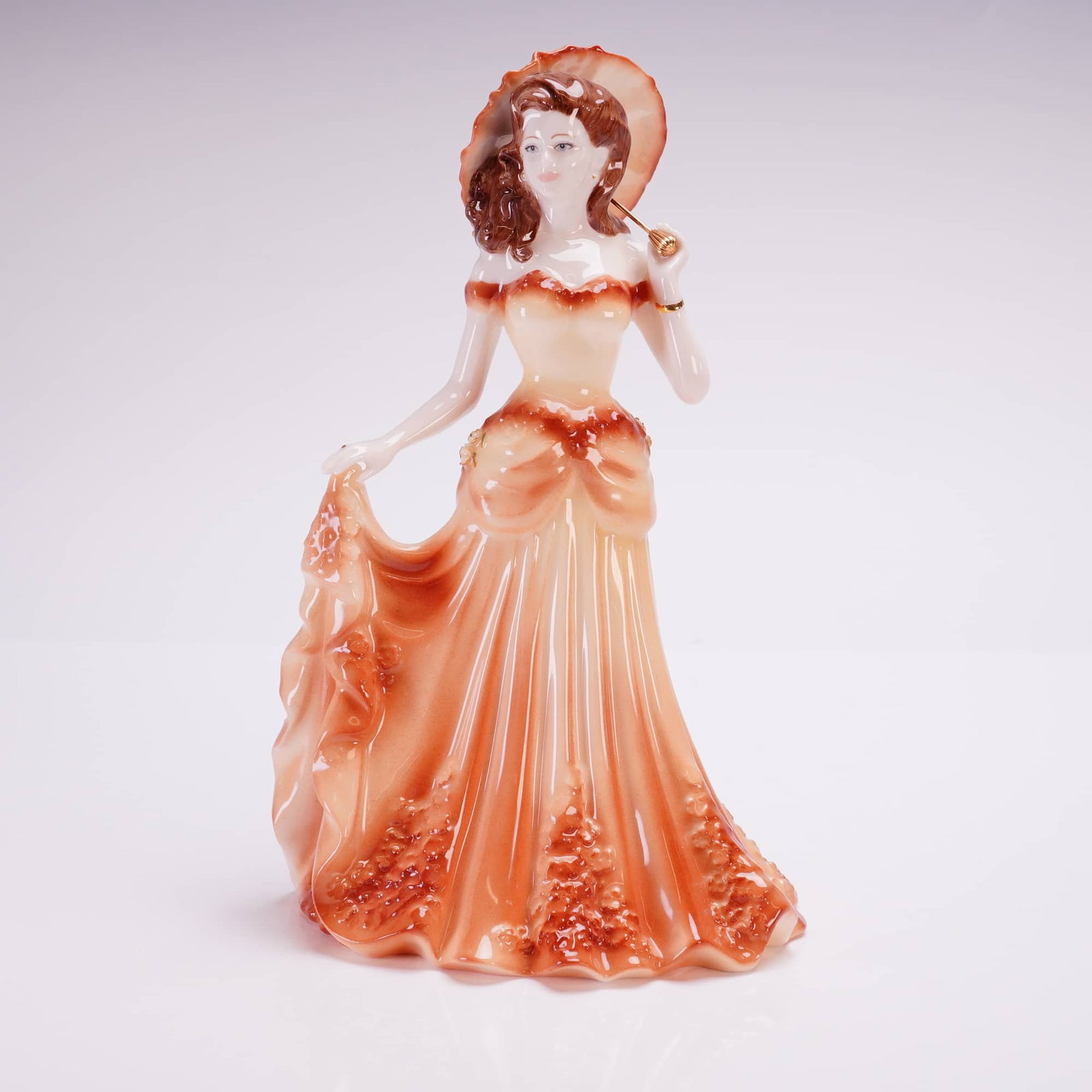 Coalport Bone China Figurine, Summertime: A Coalport figurine depicting a female figure in a tiered full-length gown and a wide-brimmed hat, holding the handle of a parasol. The piece is hand-decorated with cream and peach-orange gradient gla
