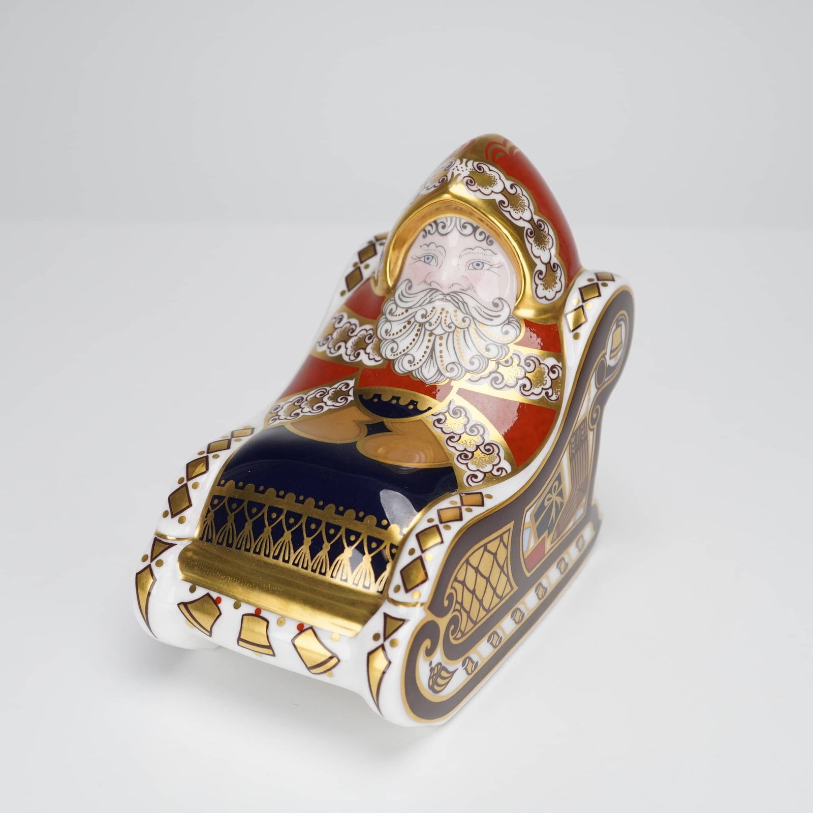Royal Crown Derby Santa and Sleigh Paperweight: A Royal Crown Derby bone china paperweight depicting Santa Claus seated in a sleigh. The figurine is decorated in a festive holiday motif utilizing deep red, blue, and brown enamels, heavily accented