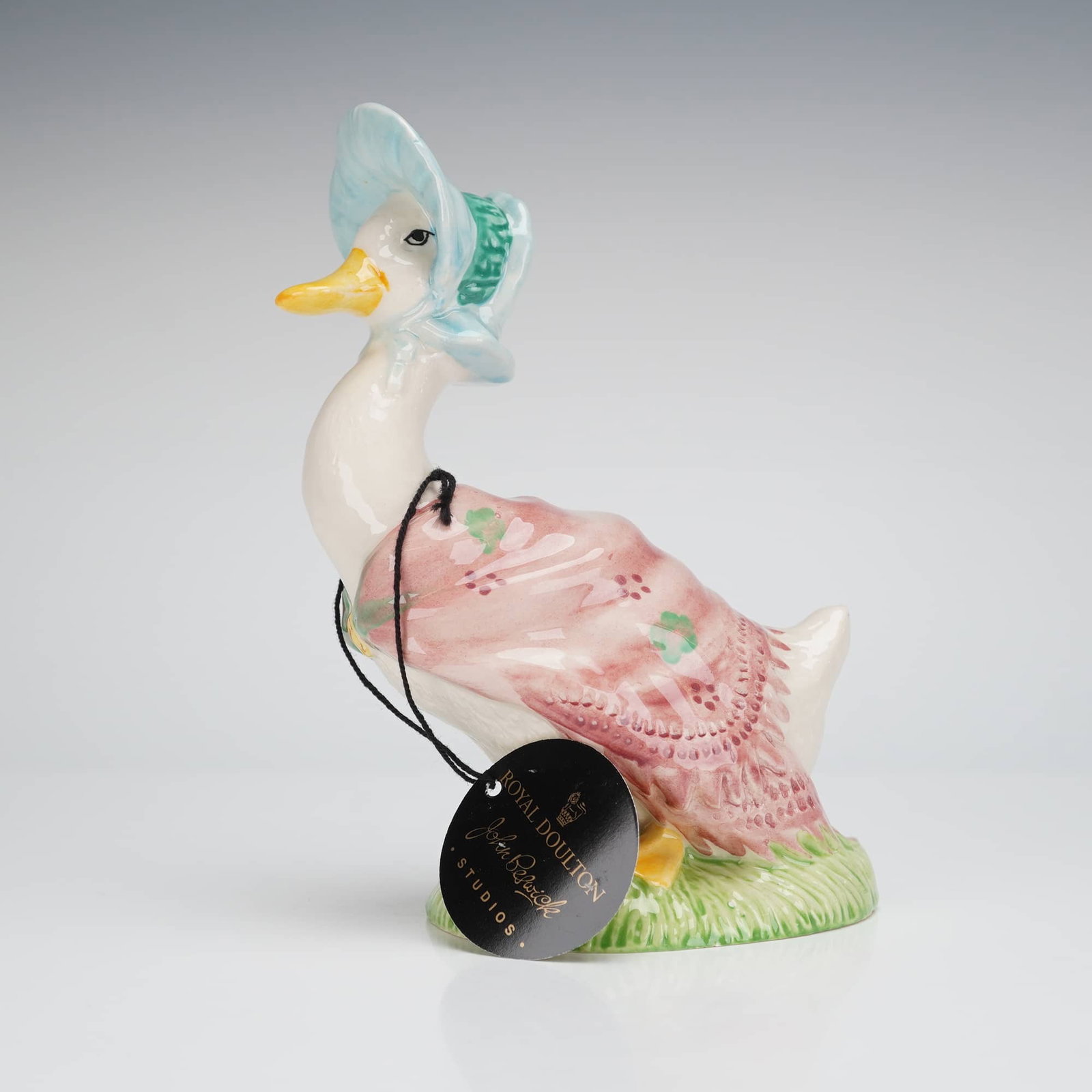 Beswick Centenary Beatrix Potter Jemima Puddle-Duck Figurine: A glazed ceramic figurine depicting the Beatrix Potter character Jemima Puddle-Duck. The figure is rendered in the Beswick style, wearing a pink shawl decorated with green clover motifs and a light bl