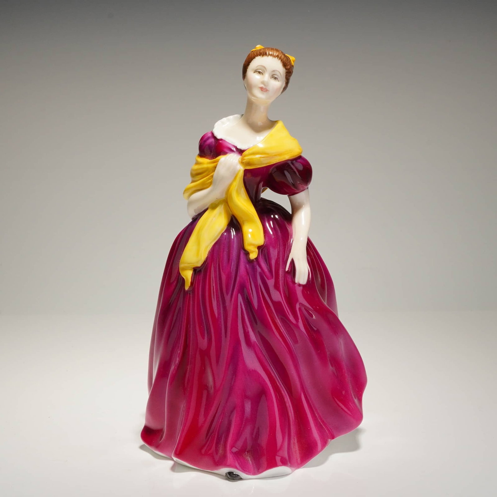 Royal Doulton Figurine Adrienne HN2152: A Royal Doulton porcelain figurine, titled "Adrienne," HN 2152. The piece is crafted from glazed, hand-painted bone china, depicting a woman in a period gown, characterized by voluminous magenta fabri
