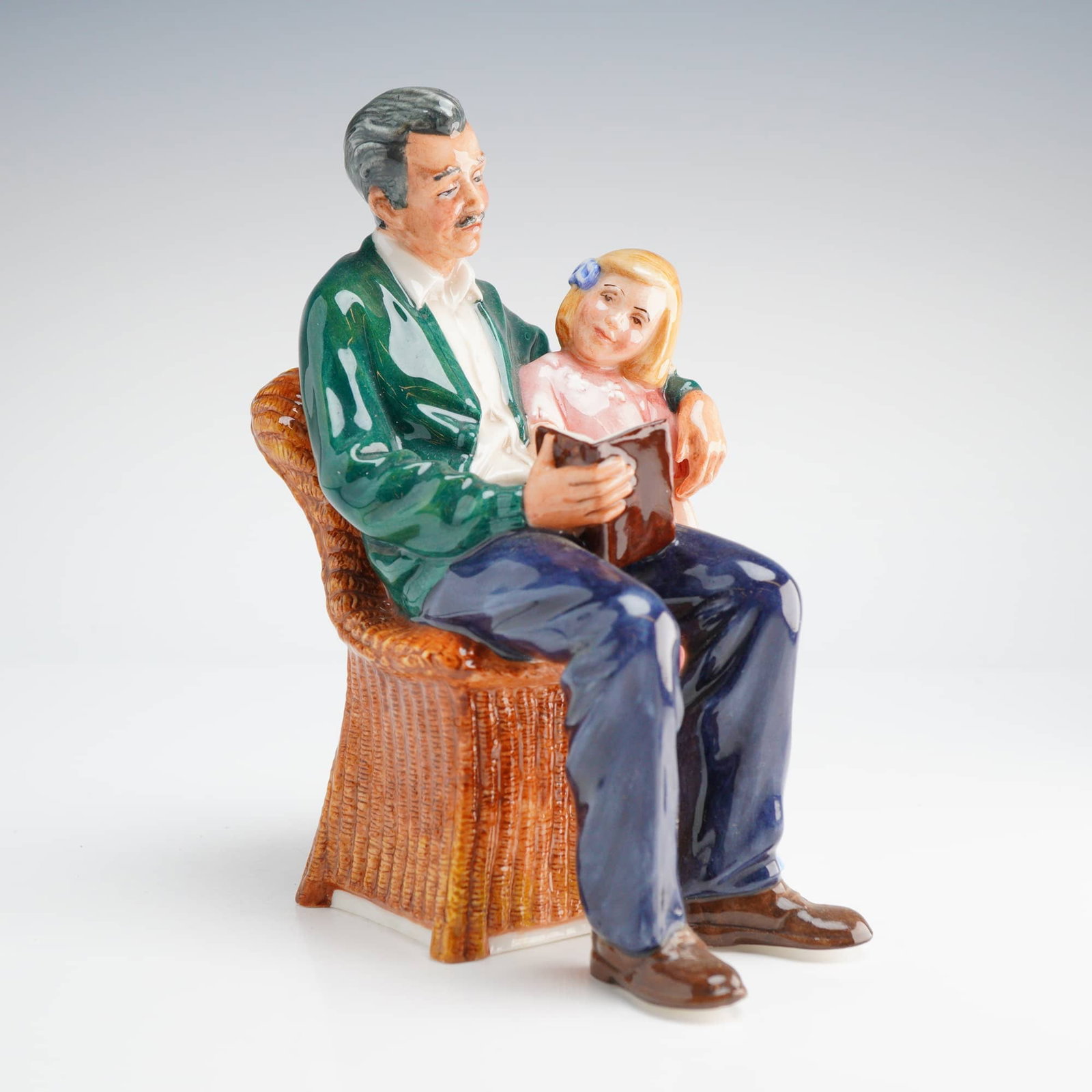 Royal Doulton Figurine Grandpa's Story HN 3456: A Royal Doulton Figurine, Grandpa's Story HN3456, copyrighted 1994, depicting a grandfather reading to a girl seated in a wicker chair, colored primarily in green, blue, pink, and brown. Dimensions: 4