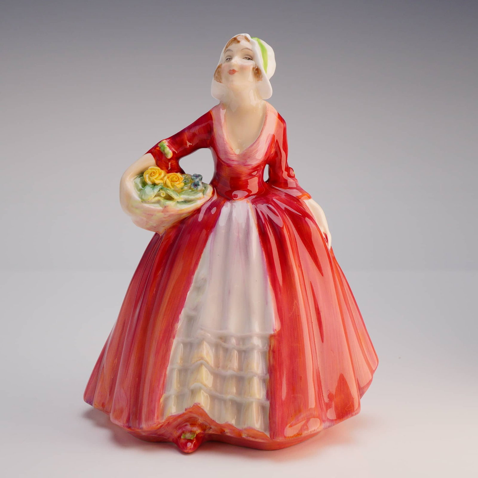 Royal Doulton Figurine Janet HN1537: The figurine depicts a standing female figure in period dress, copyrighted 1932. The figure is characterized by a voluminous, flowing skirt painted primarily in deep, glossy red over a pale yellow and