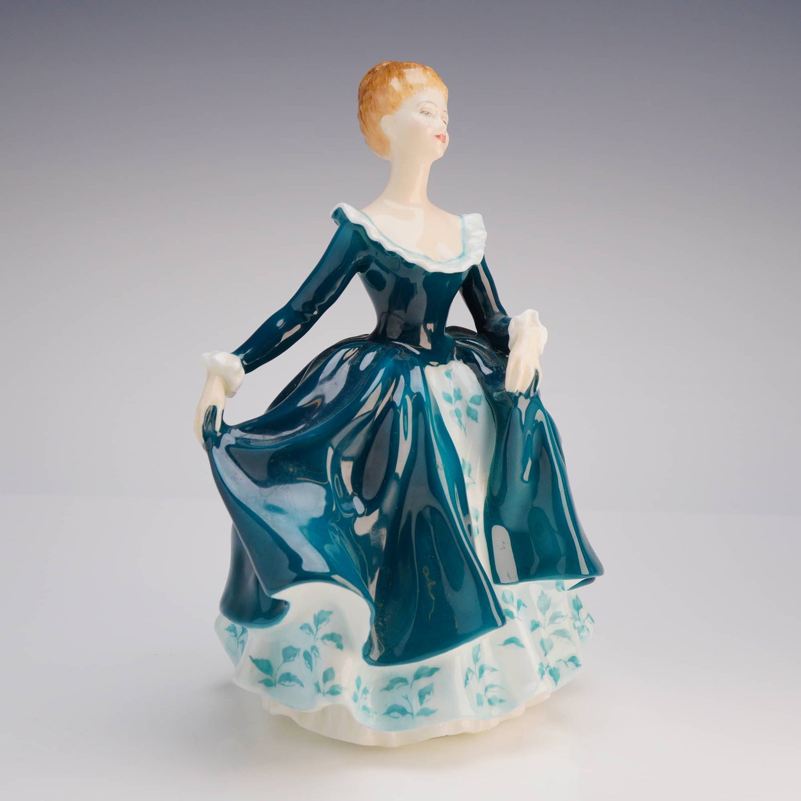 Royal Doulton Figurine Janine HN 2461: A single bone china figurine manufactured by Royal Doulton, identified as the model Janine, HN 2461. The figure depicts a standing woman with reddish-blonde hair, dressed in a long, layered gown. The