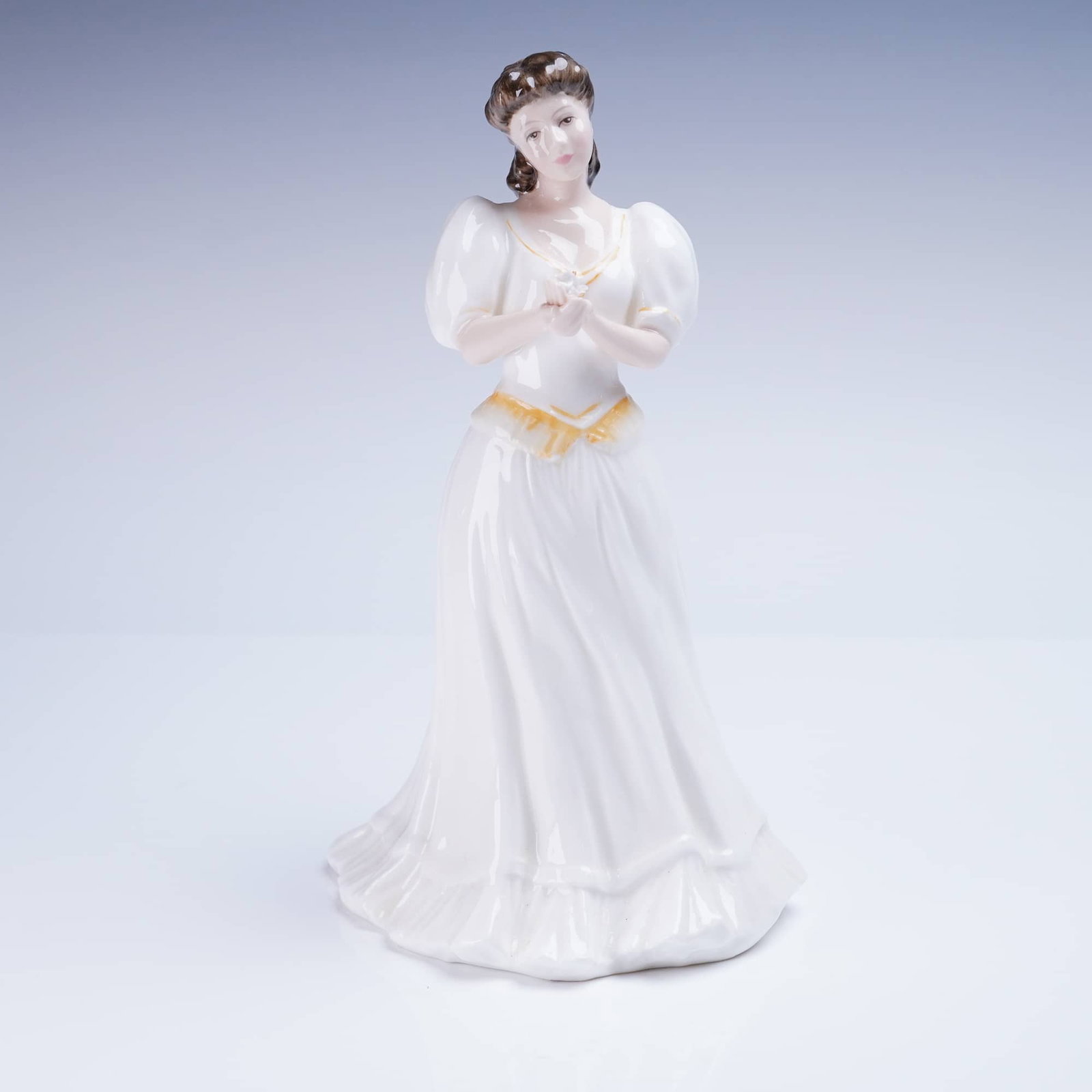 Royal Doulton Figurine Maria HN 3381: A glazed porcelain figurine by Royal Doulton, titled Maria, model number HN 3381. The figure depicts a standing female figure dressed in a long white gown featuring puffed sleeves. The gown is accente