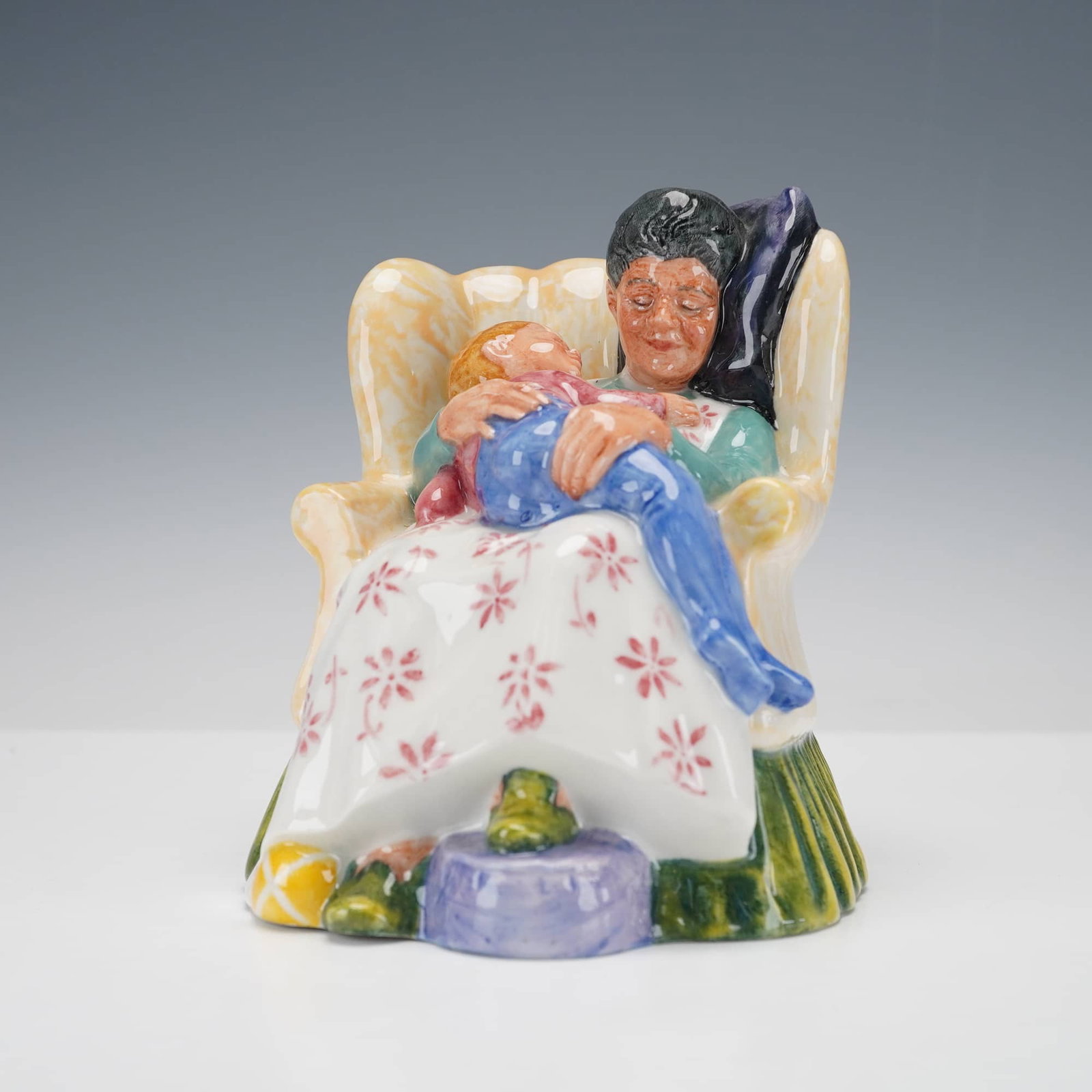 Royal Doulton Figurine, Sweet Dreams HN2380: A wholesome hand-painted porcelain figurine depicting a tender domestic scene of a woman seated in an upholstered armchair with a young child peacefully asleep in her arms. The figure showcases rich c