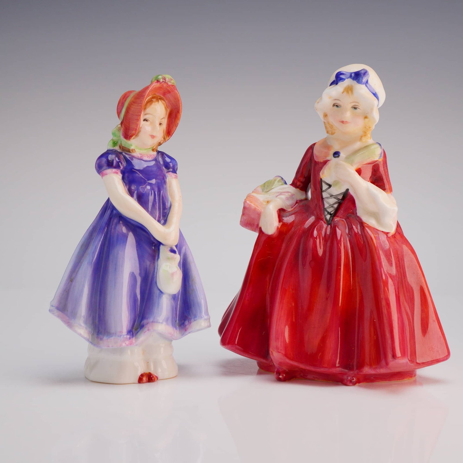 2pc Royal Doulton Figurines, Lavinia HN 1955 and Ivy HN 1768: The lot includes the figure Lavinia (HN 1955, COPR 1940), depicted in a vivid red gown and white cap, and the figure Ivy (HN 1768, COPR 1936), dressed predominantly in a purple gown and red hat. Both