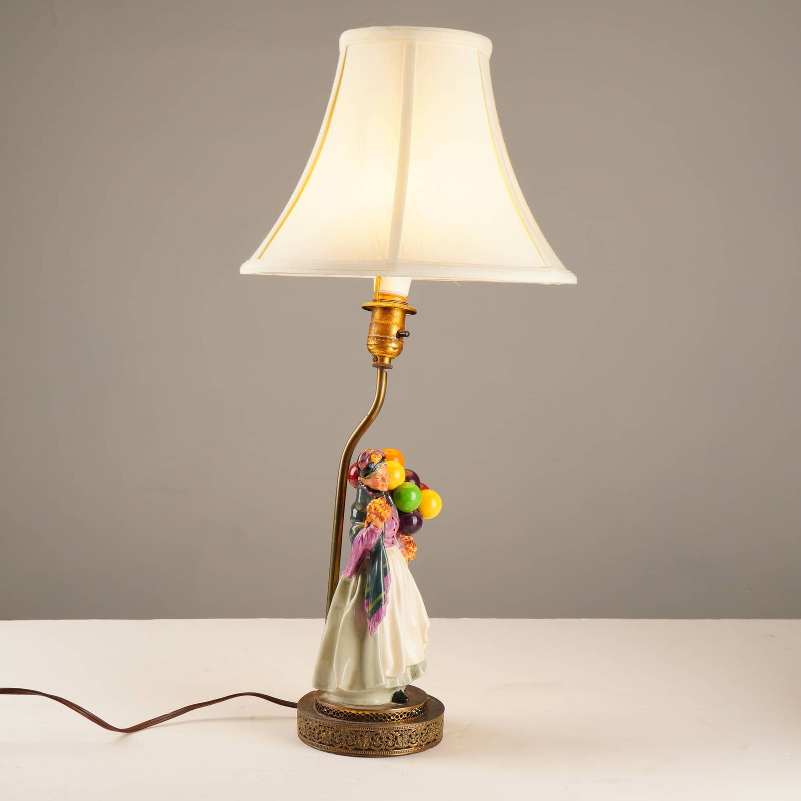 Royal Doulton Balloon Lady HN 1843 Porcelain Figurine Table Lamp: A table lamp featuring a Royal Doulton porcelain figurine titled Biddy Pennyfarthing, or the Balloon Lady, model HN 1843, designed by Leslie Harradine. The hand-painted, glazed ceramic figure depicts