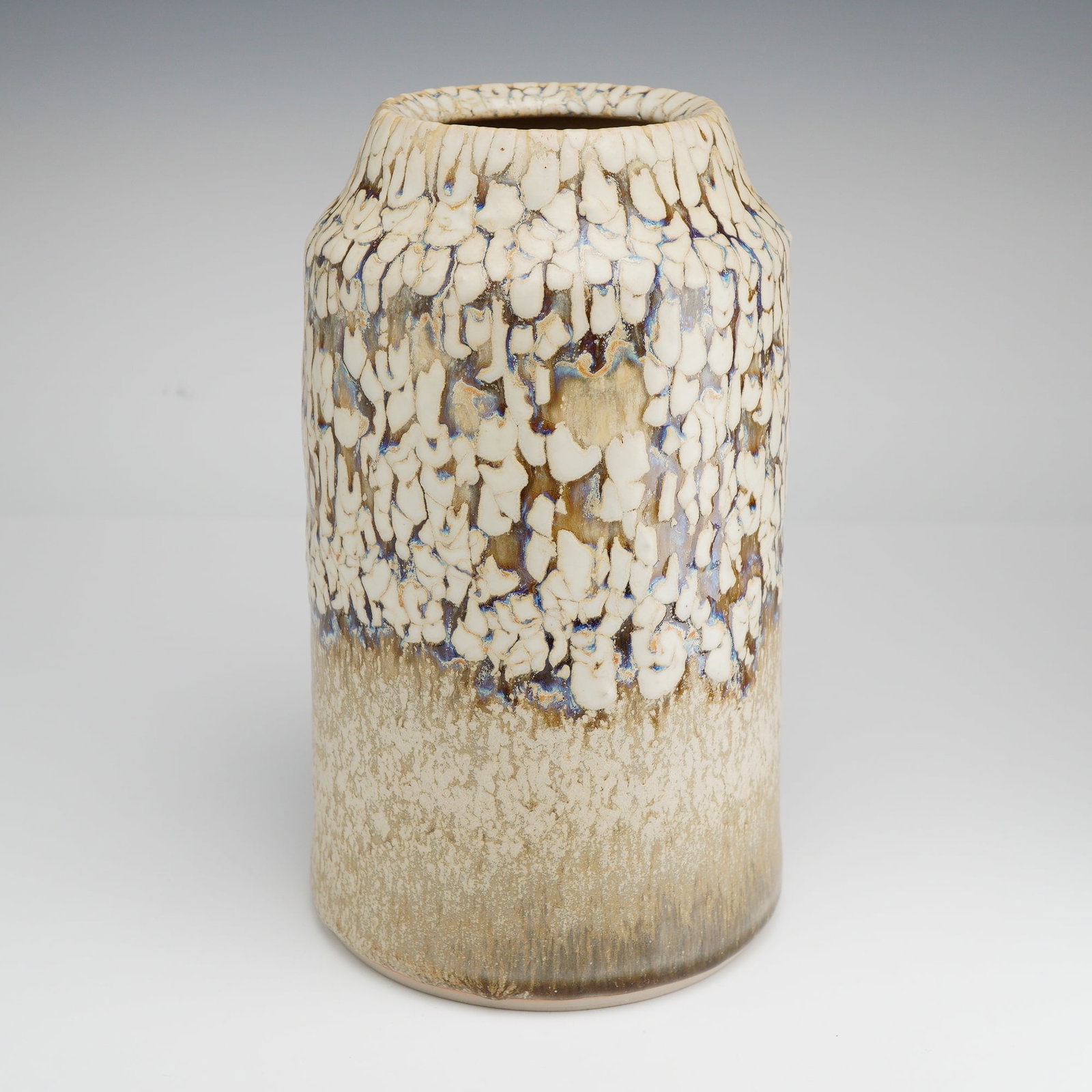 Mid-Century Modernist Studio Pottery Vase: Vase of cylindrical form with a slightly tapered neck. The vessel features a multi-tonal, textured glaze treatment. The upper section is decorated with a thick, white crawl fat lava glaze, exhibiting