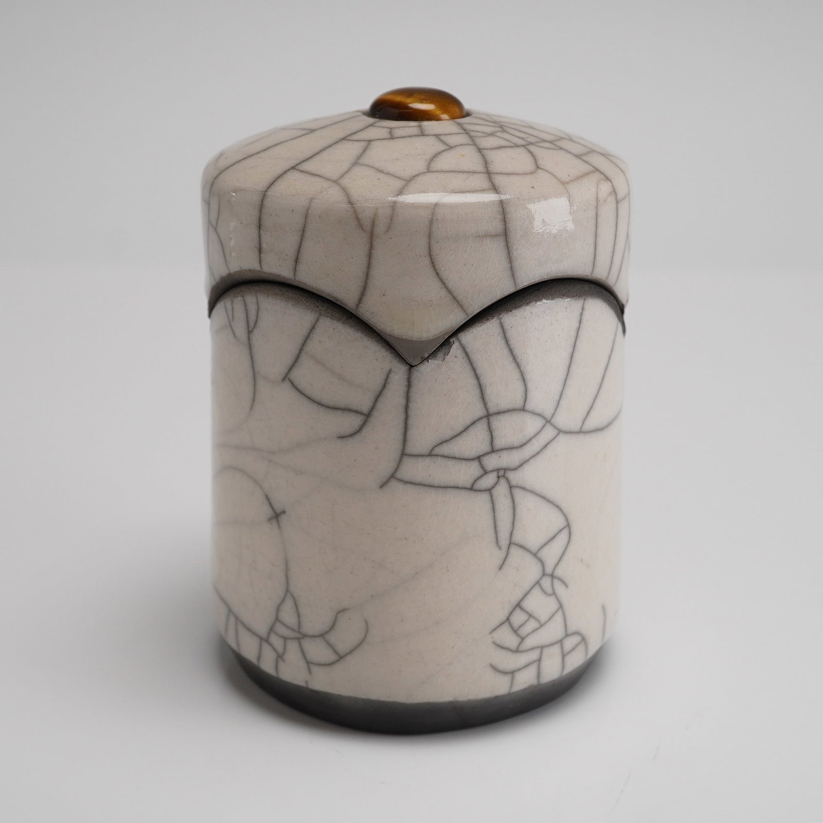 Raku Crackle Glaze Lidded Studio Pottery Box Signed: A single cylindrical Raku fired studio pottery box with lid. The vessel is finished with a thick, glossy, pale beige crackle glaze, where the deep fissures have been intentionally stained dark gray or