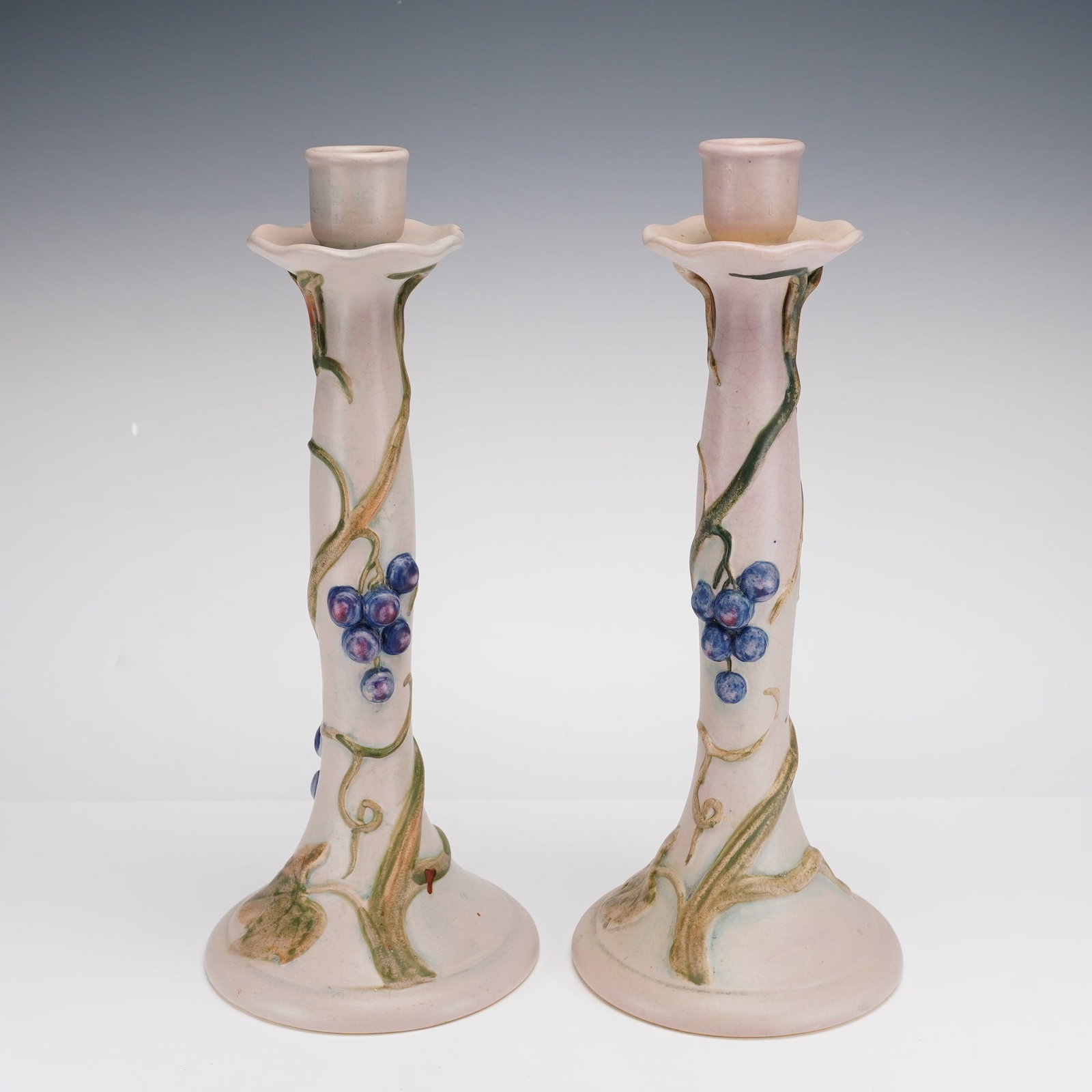 A Pair of Weller Melrose Art Pottery Candlesticks: This pair of Weller Melrose candlesticks is crafted from fine earthenware art pottery. Introduced circa 1915, the Melrose pattern is characterized by its Art Nouveau-inspired trailing grapevine motif.