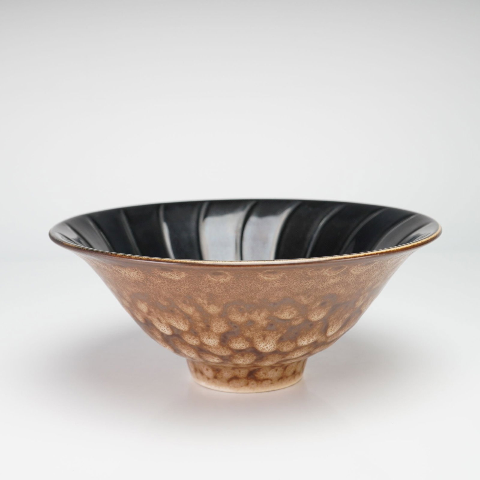 Wedgwood Norman Wilson Experimental Glaze Conical Bowl from the Rubin Collection: This fine stoneware bowl was manufactured by Wedgwood in England and designed by Norman Wilson. The piece features a flared, conical form resting on a small circular foot. The interior surface is mold